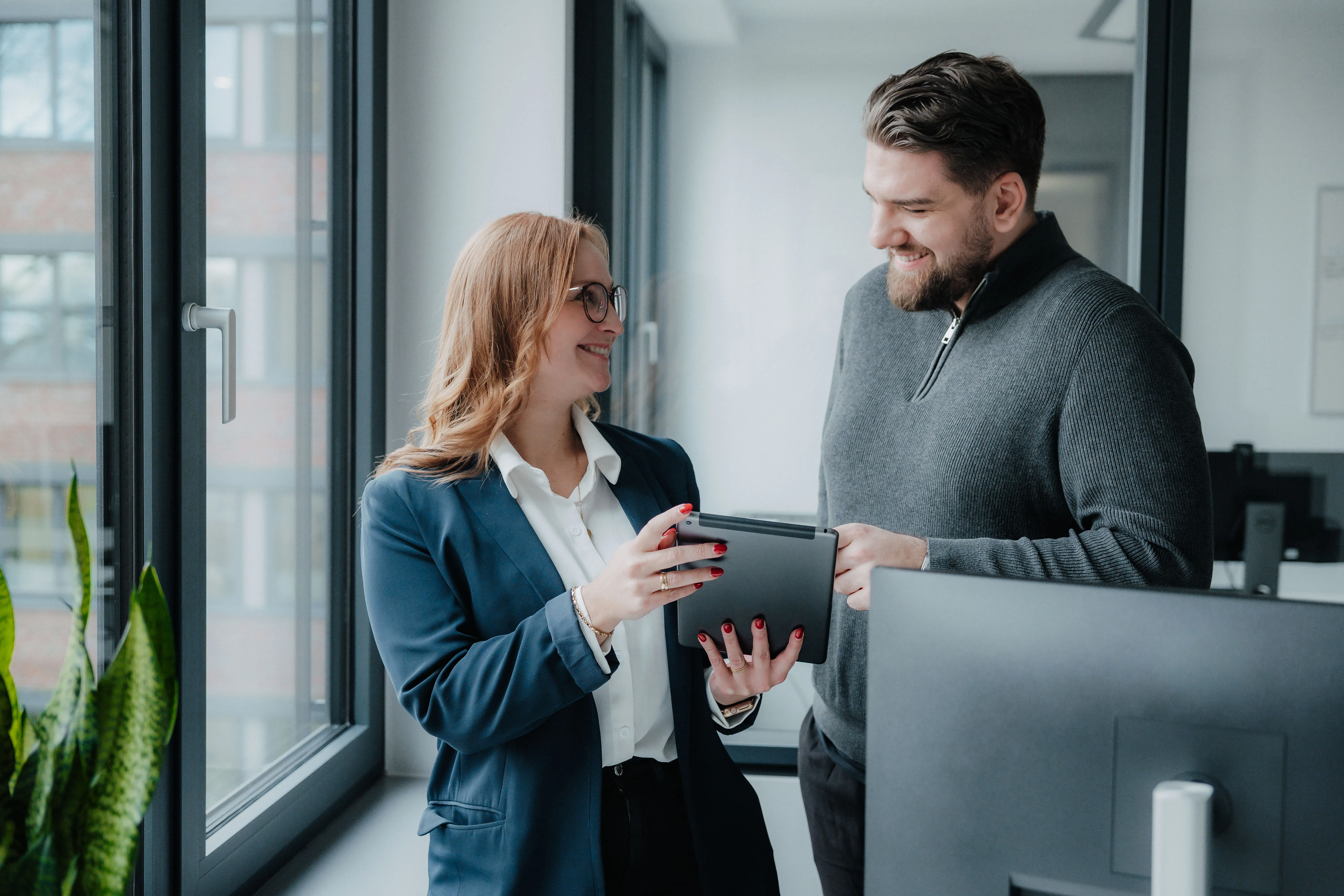Zwei Kollegen im modernen Büro tauschen sich freundlich über ein Tablet aus – werde Teil des Teams bei SARIA!