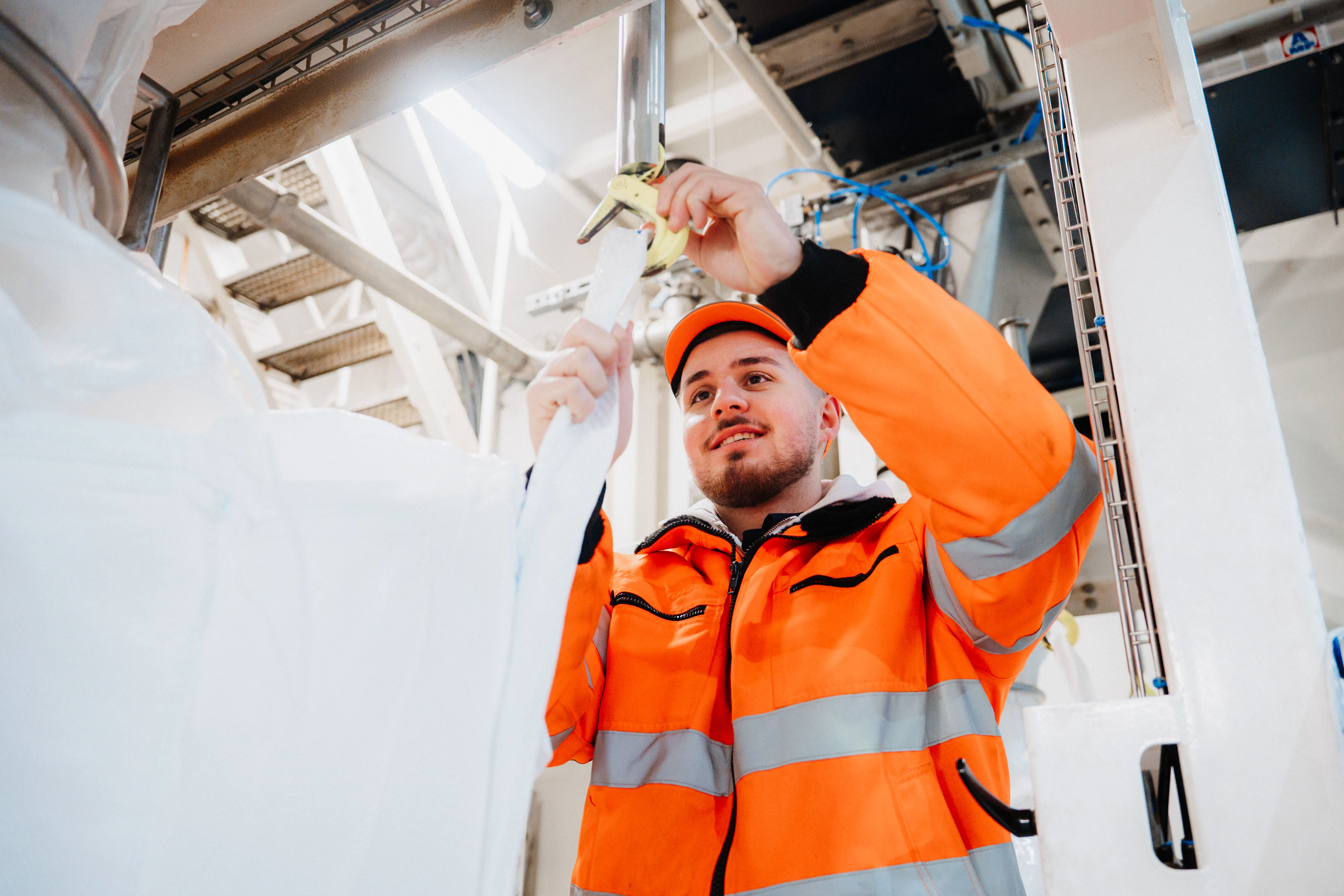Ein Mitarbeiter in orangefarbener Schutzkleidung befestigt einen Sack an einer Industrieanlage bei SARIA.