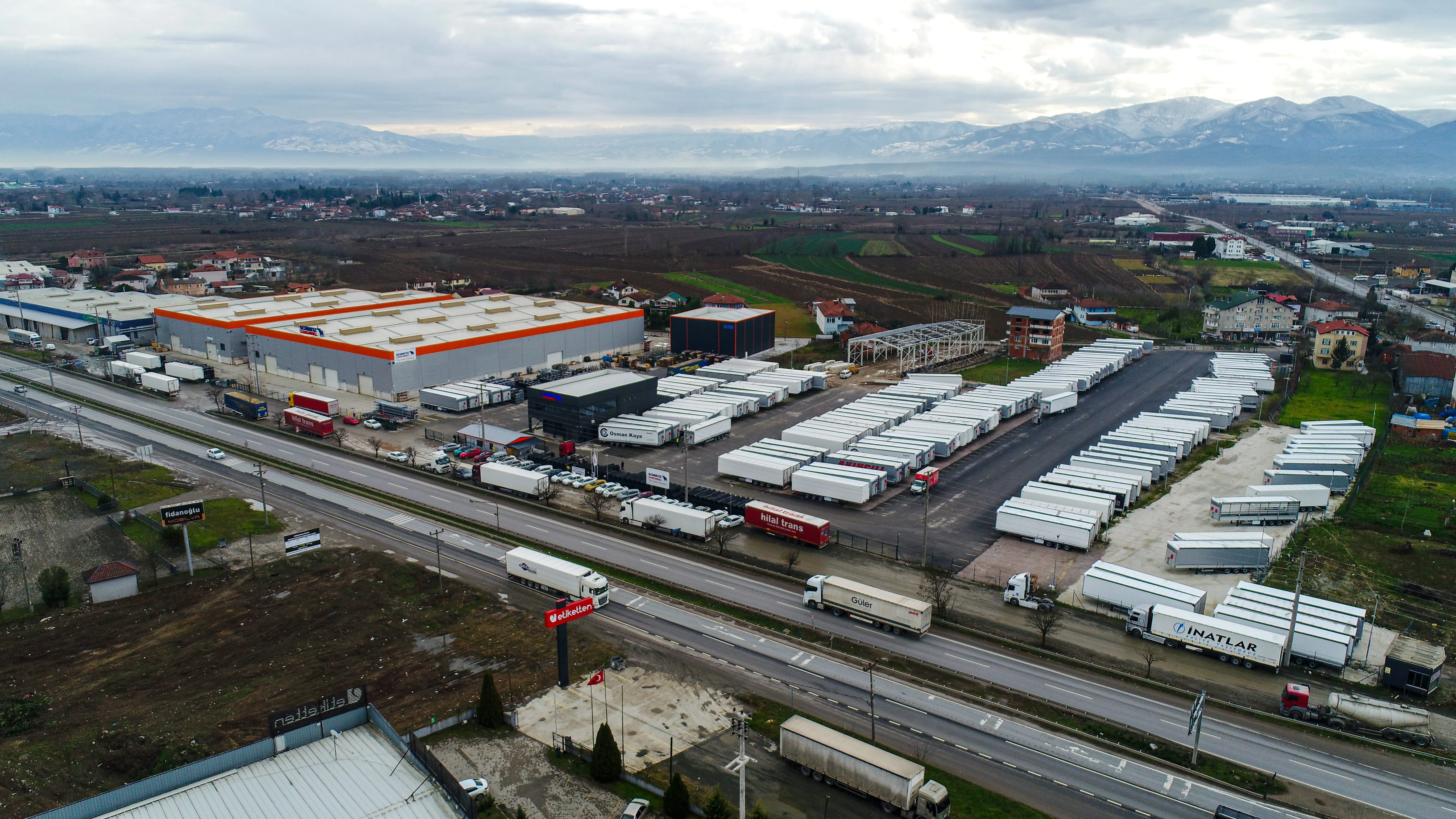 Aerial view of Schmitz Cargobull AG facility with rows of parked trailers and trucks, set against a scenic mountain backdrop.