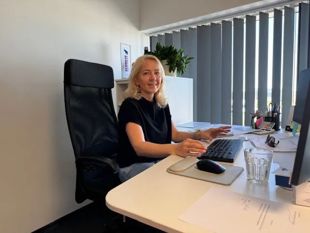 A friendly employee at Schmitz Cargobull AG working at her desk, smiling and engaging with her computer in a bright office.