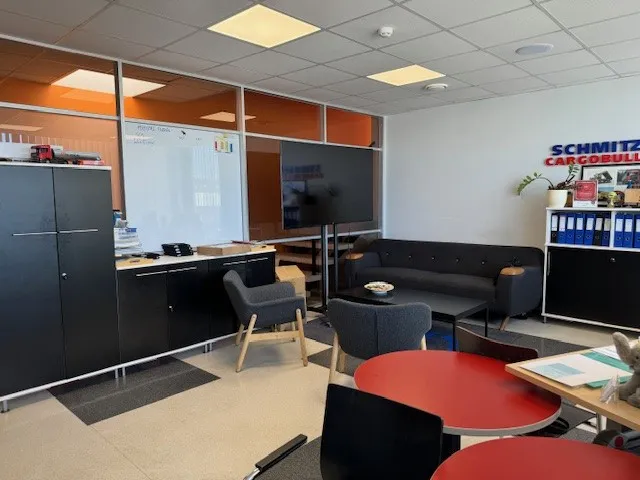 A cozy office space at Schmitz Cargobull AG with modern furniture, a TV, and a touch of greenery.