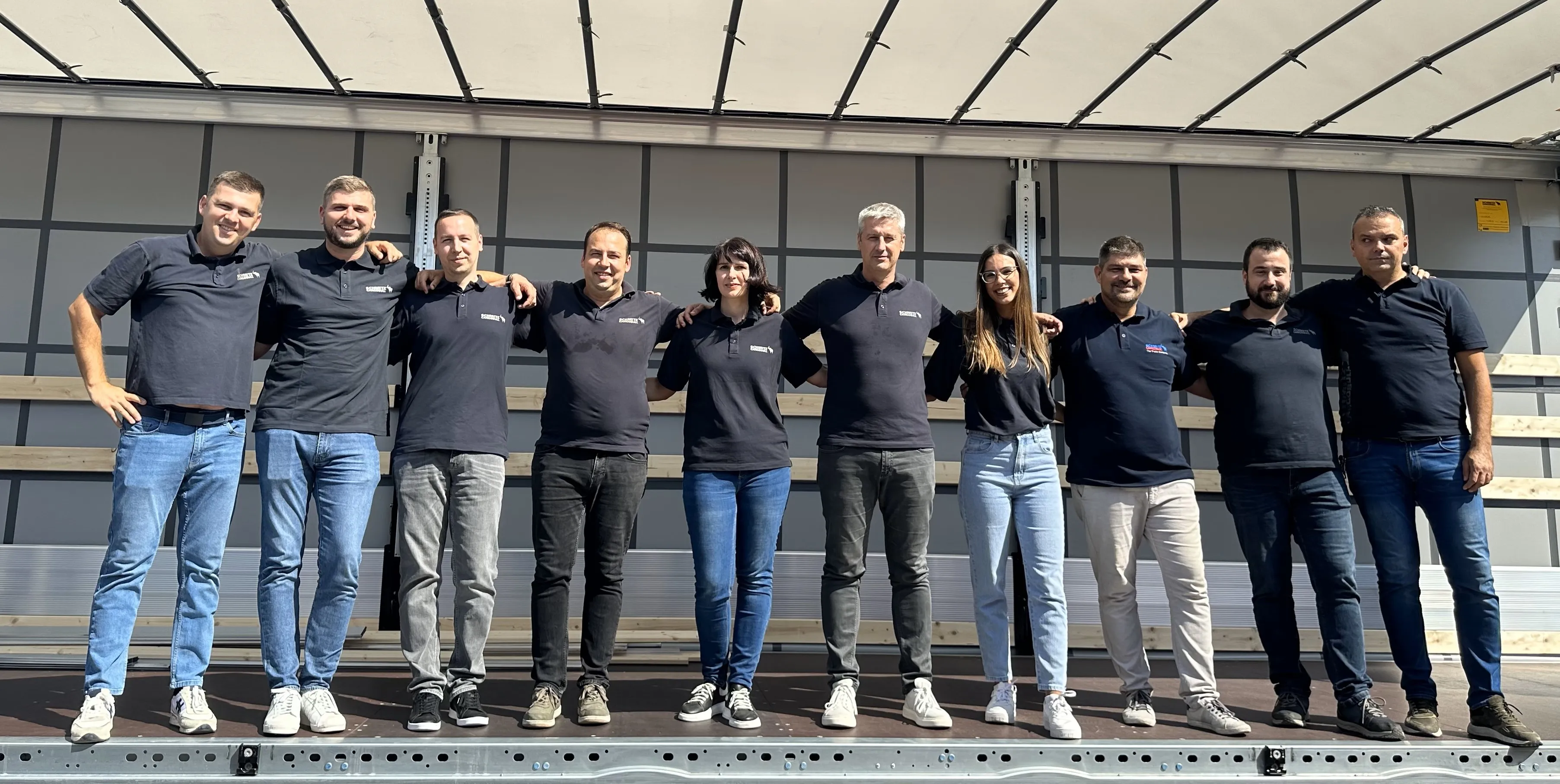 Team Schmitz Cargobull AG standing together, smiling in casual attire, showcasing camaraderie and team spirit in the automotive industry.