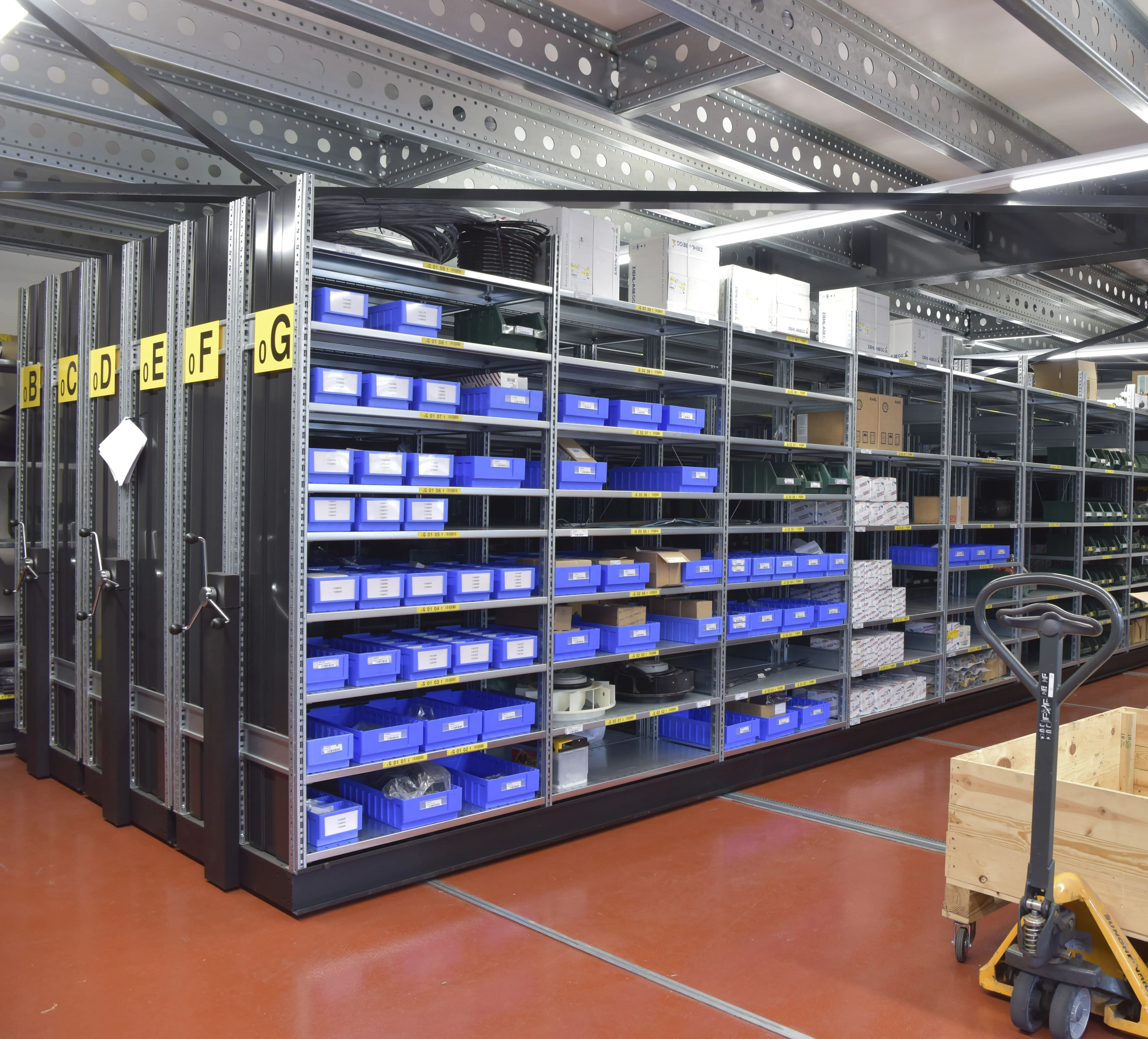 Modern warehouse setup at Schmitz Cargobull AG with organized shelves of blue bins, a wooden crate, and a pallet jack.