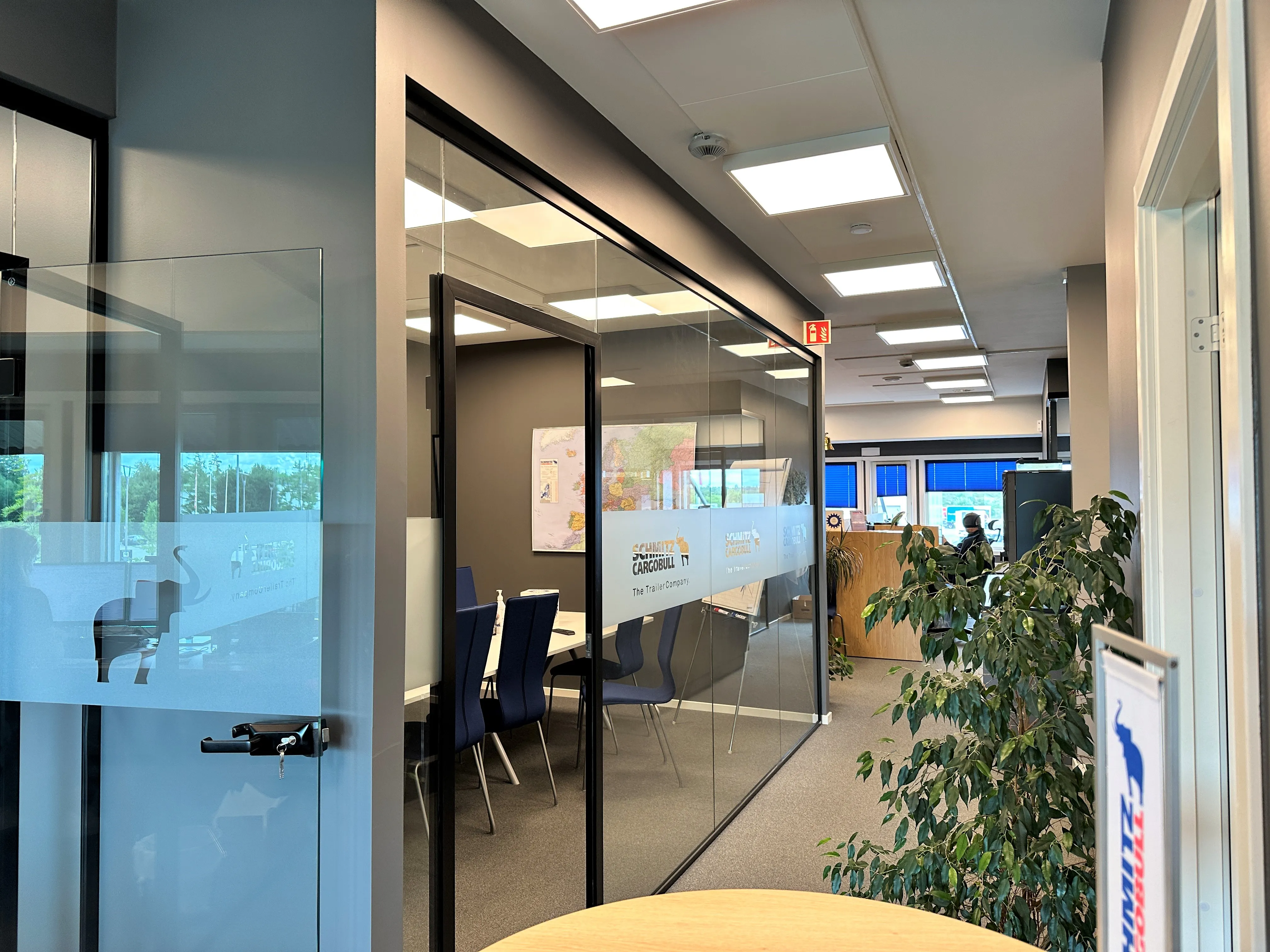 Modern office hallway at Schmitz Cargobull AG with glass-walled meeting rooms and blue chairs, reflecting a vibrant work environment.