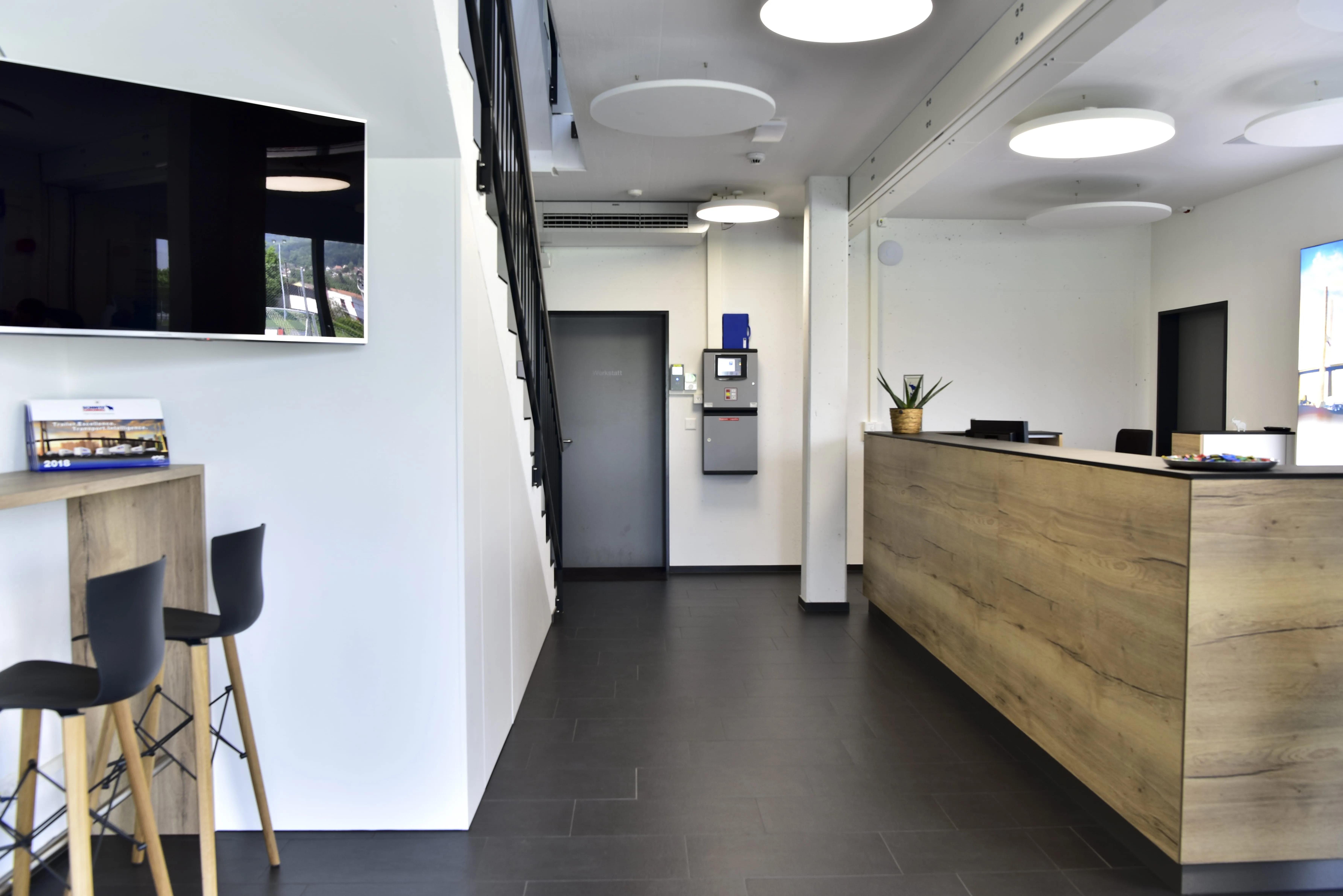 A modern and welcoming reception area at Schmitz Cargobull AG, featuring a sleek wooden desk, seating, and a wall-mounted TV.