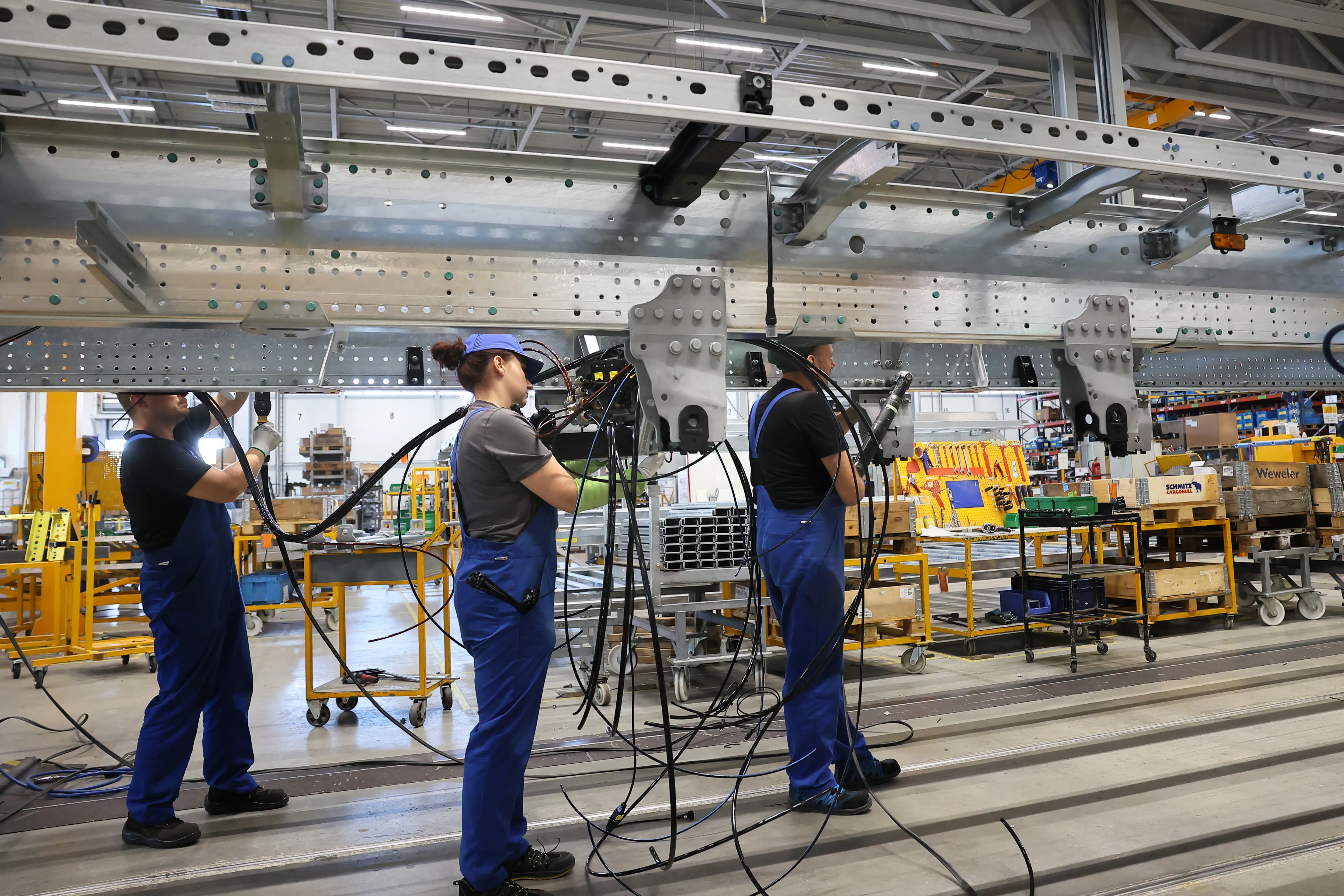 Workers in blue overalls assembling a large trailer component at Schmitz Cargobull AG's factory floor.