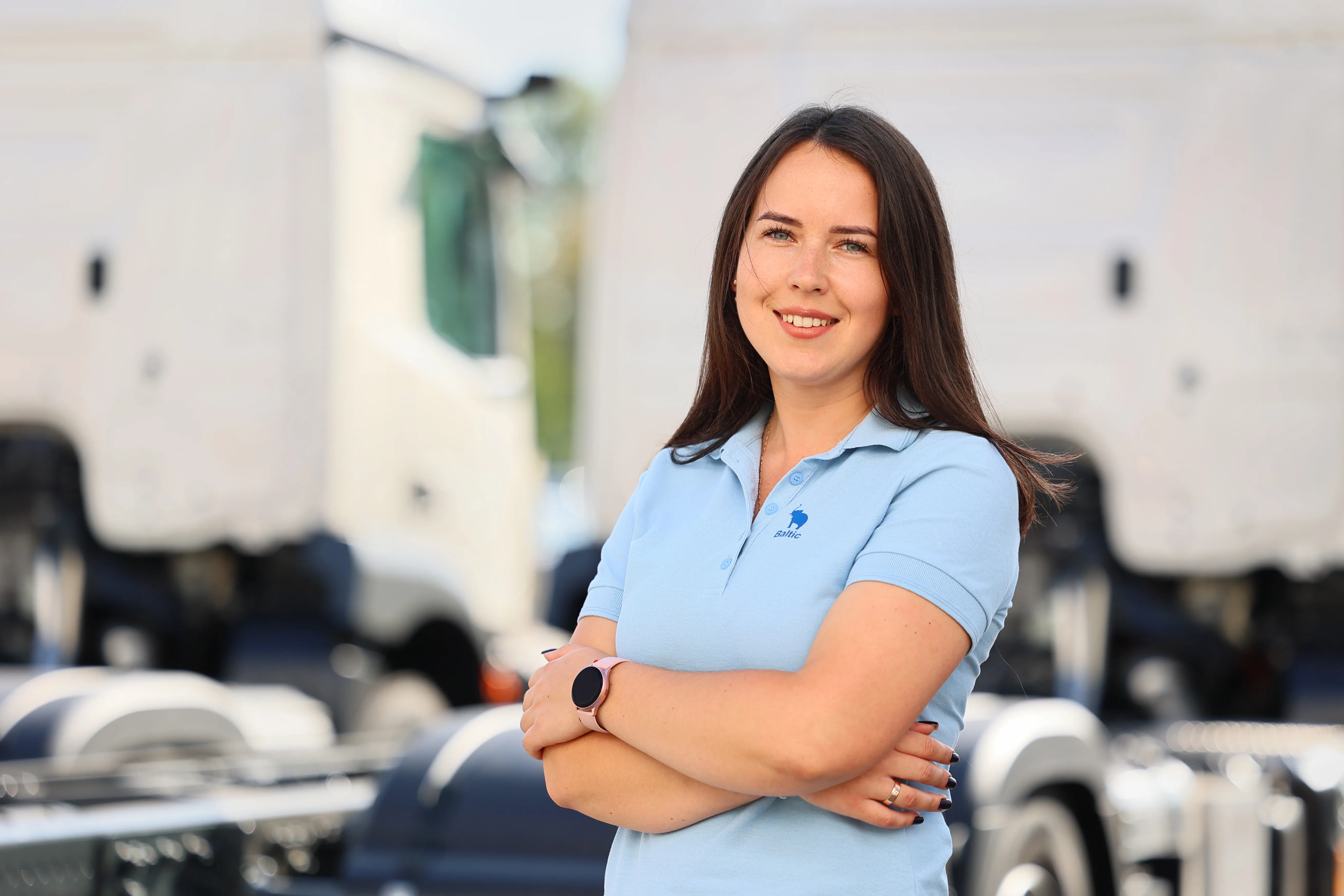A smiling woman in a Schmitz Cargobull polo stands confidently in front of a truck.