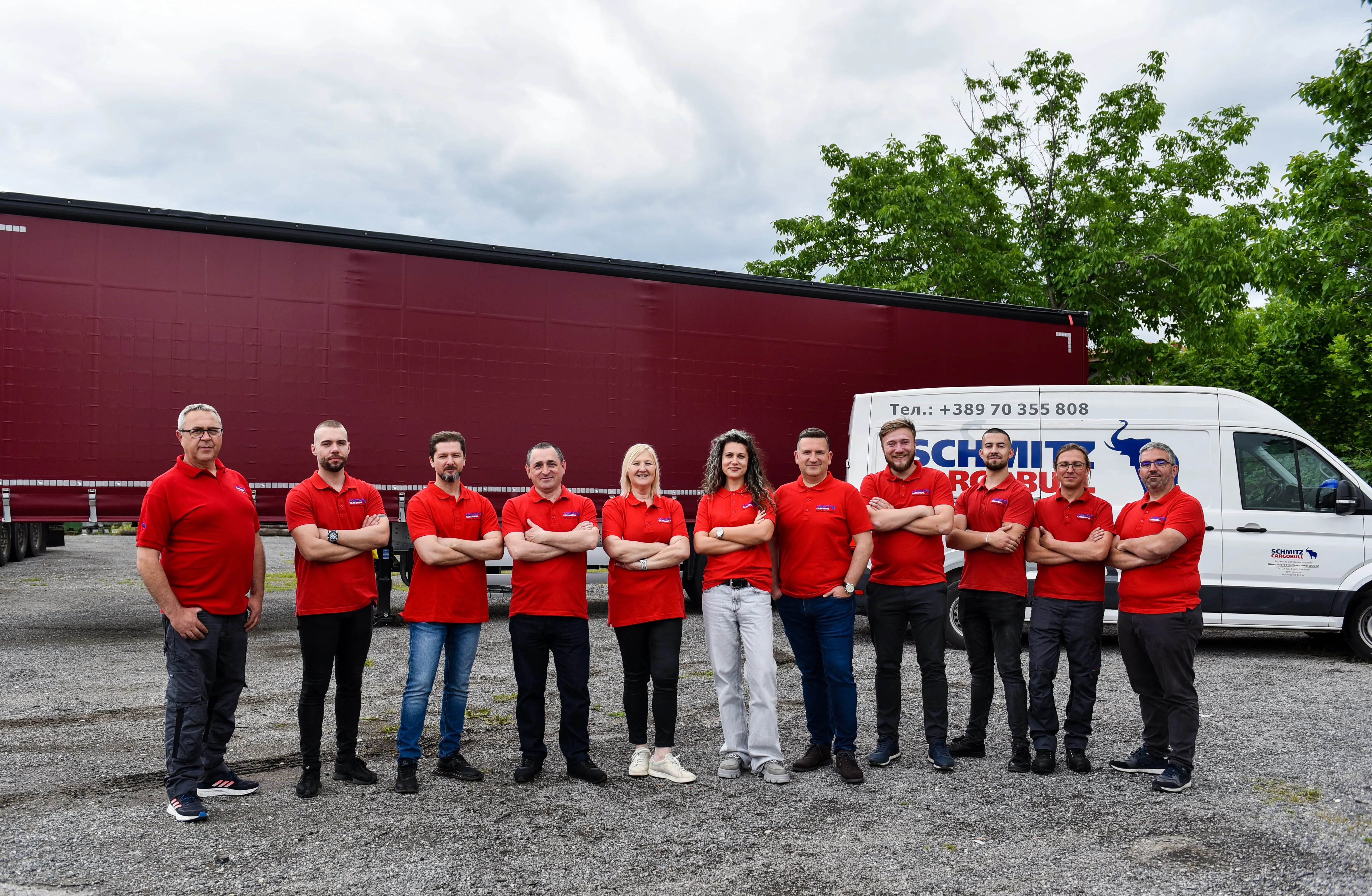 A cheerful Schmitz Cargobull team poses in front of a trailer and company van, rocking their matching red shirts.