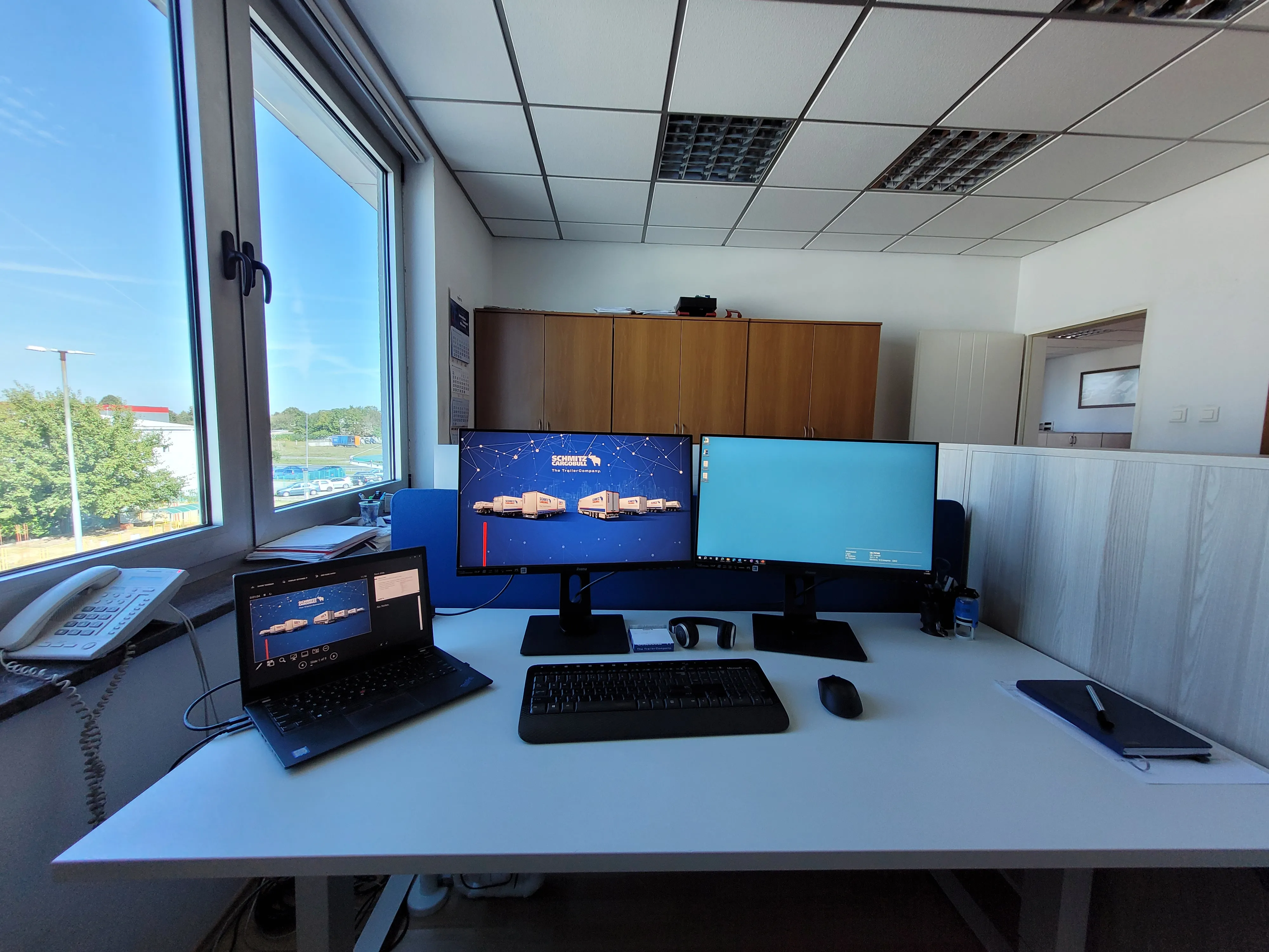Modern office hallway at Schmitz Cargobull AG with glass-walled meeting rooms and blue chairs, reflecting a vibrant work environment.