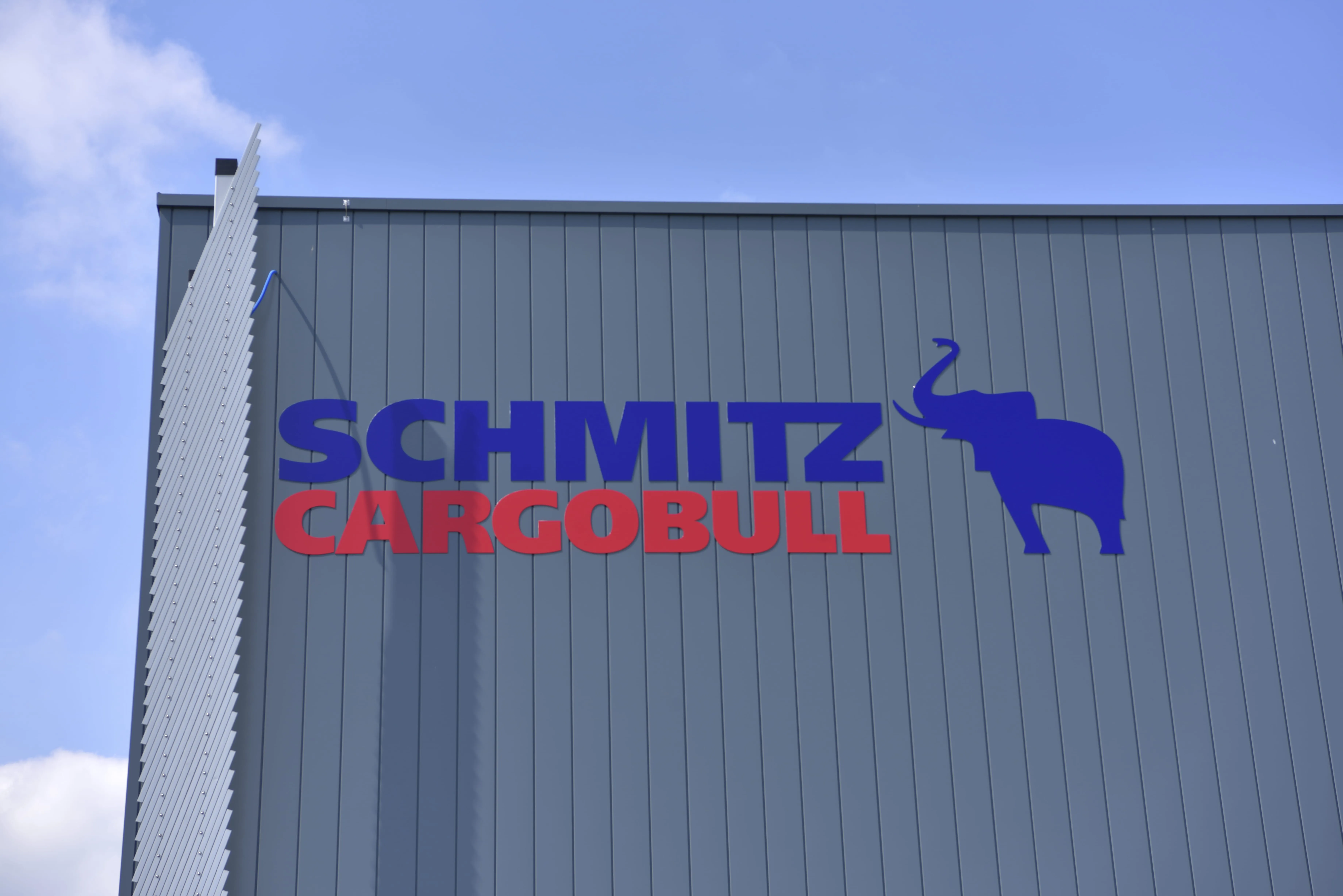 Schmitz Cargobull AG logo on a gray building facade with a blue elephant icon, against a clear sky.