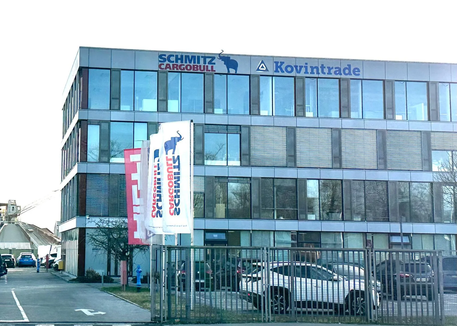Modern Schmitz Cargobull AG office building with company flags waving out front, showcasing their automotive presence.