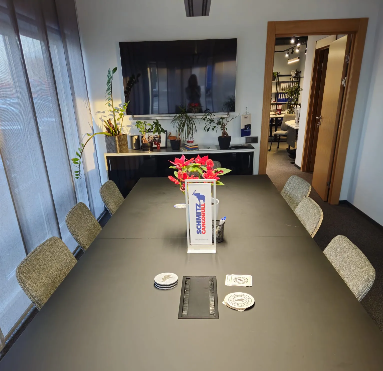 A modern Schmitz Cargobull AG conference room, featuring a sleek table, comfy chairs, plants, and a large screen.