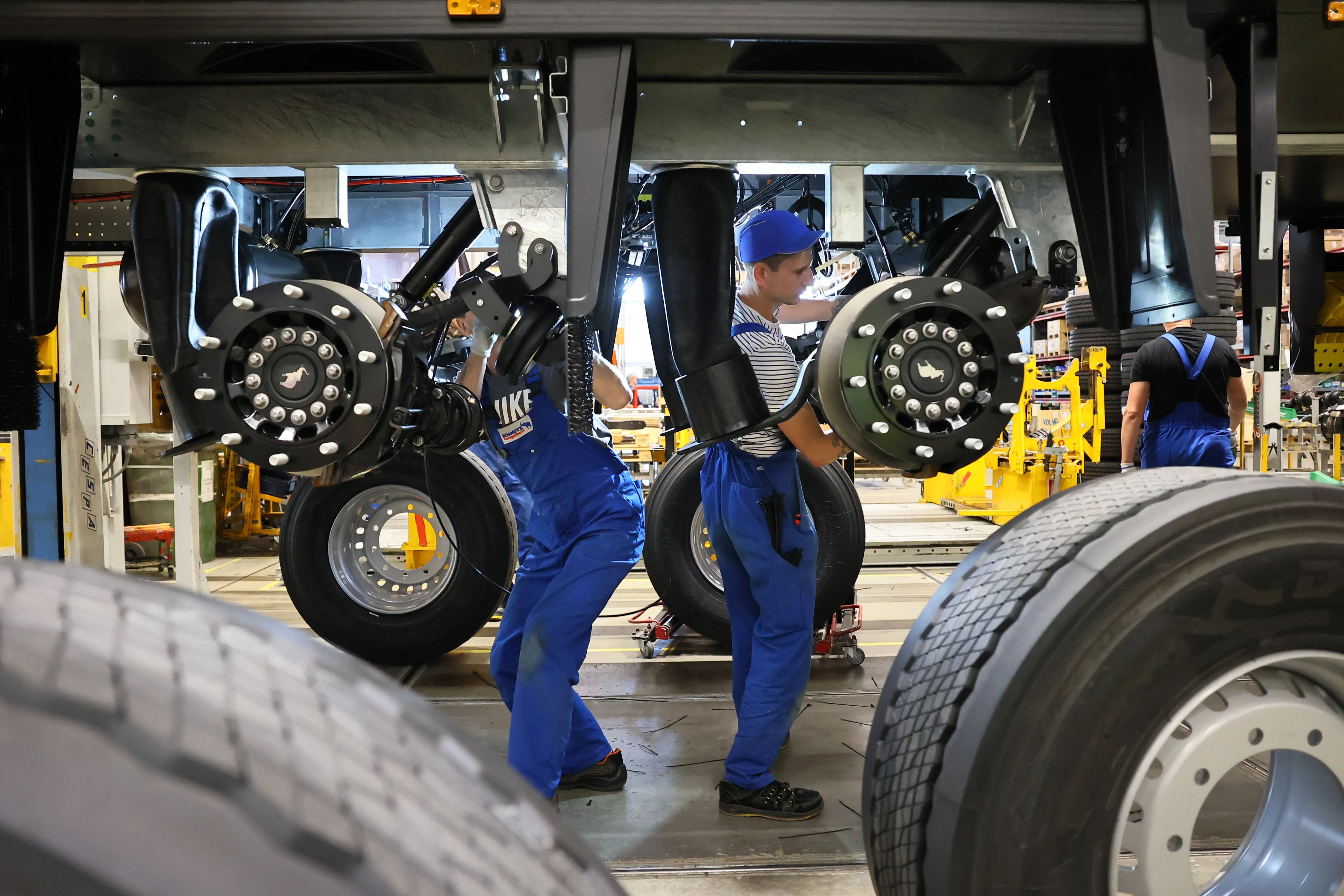 Workers in blue overalls assembling truck parts at Schmitz Cargobull AG's automotive plant.