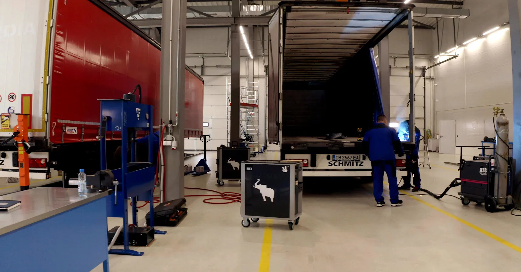 A technician in blue overalls works on a Schmitz Cargobull trailer in a modern automotive workshop.