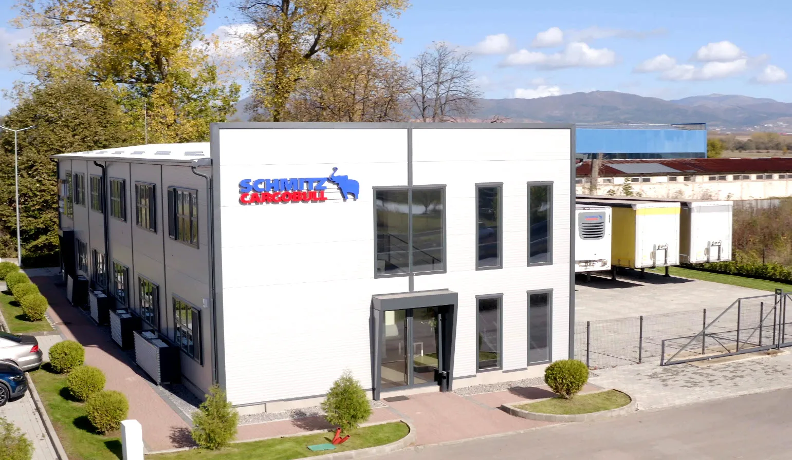 Modern Schmitz Cargobull AG office building with parked trailers, set in a scenic landscape with mountains in the background.