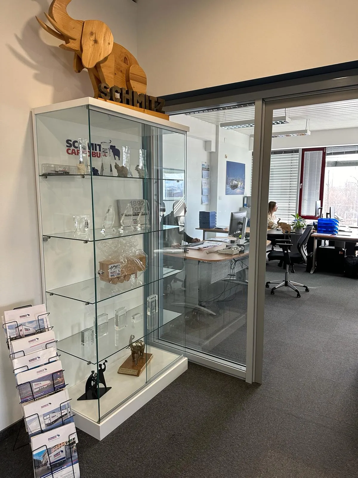 A peek into the Schmitz Cargobull AG office: trophy cabinet and a glimpse of a focused team member at work.