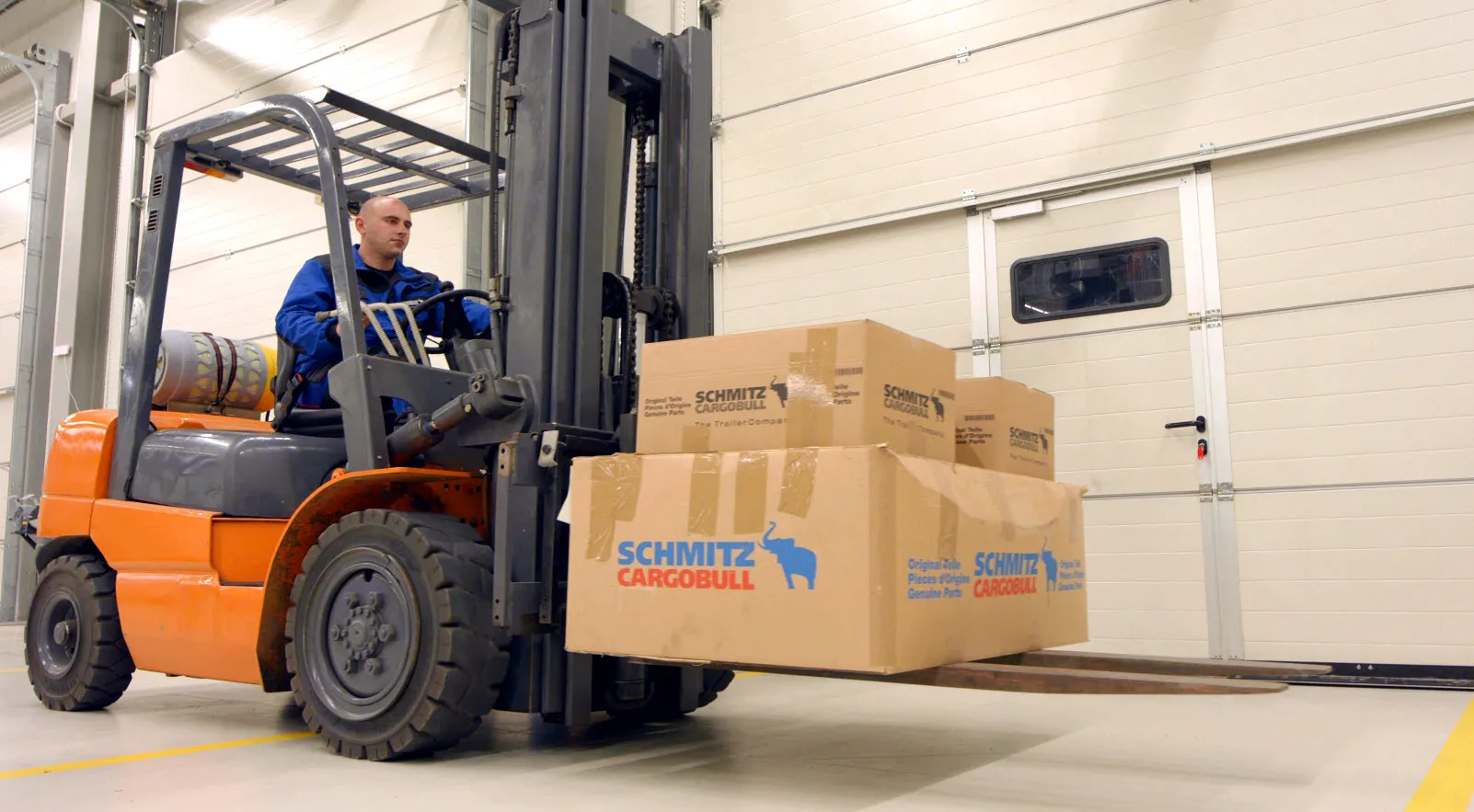 A worker skillfully operates a forklift, moving Schmitz Cargobull boxes in a warehouse.