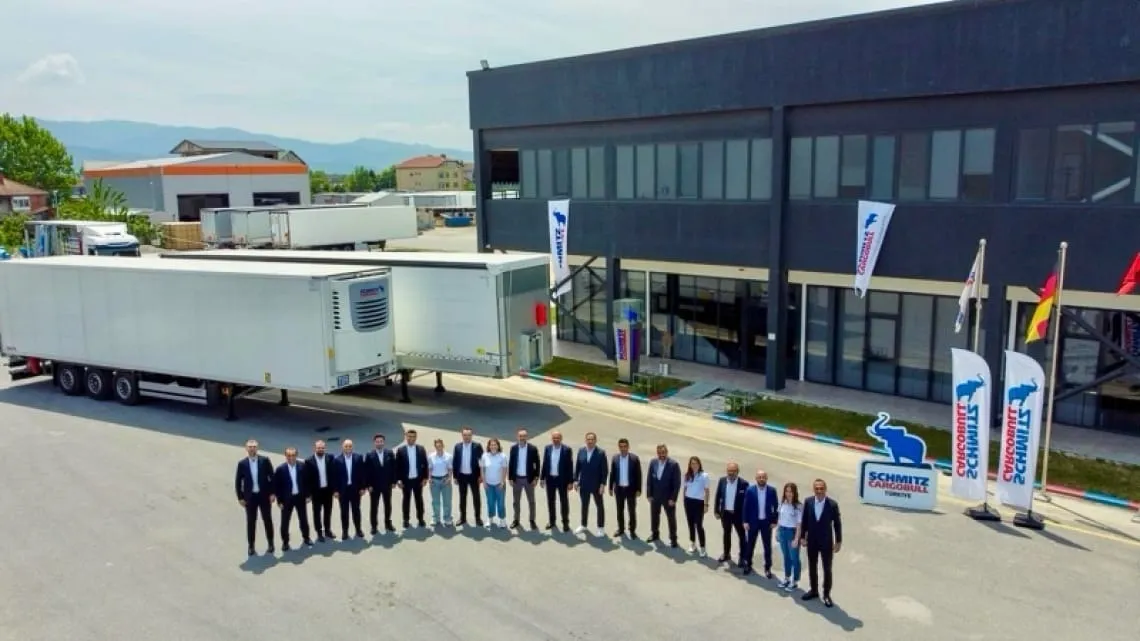 A cheerful Schmitz Cargobull team stands outside the office, showcasing a trailer, ready to roll into the automotive world.