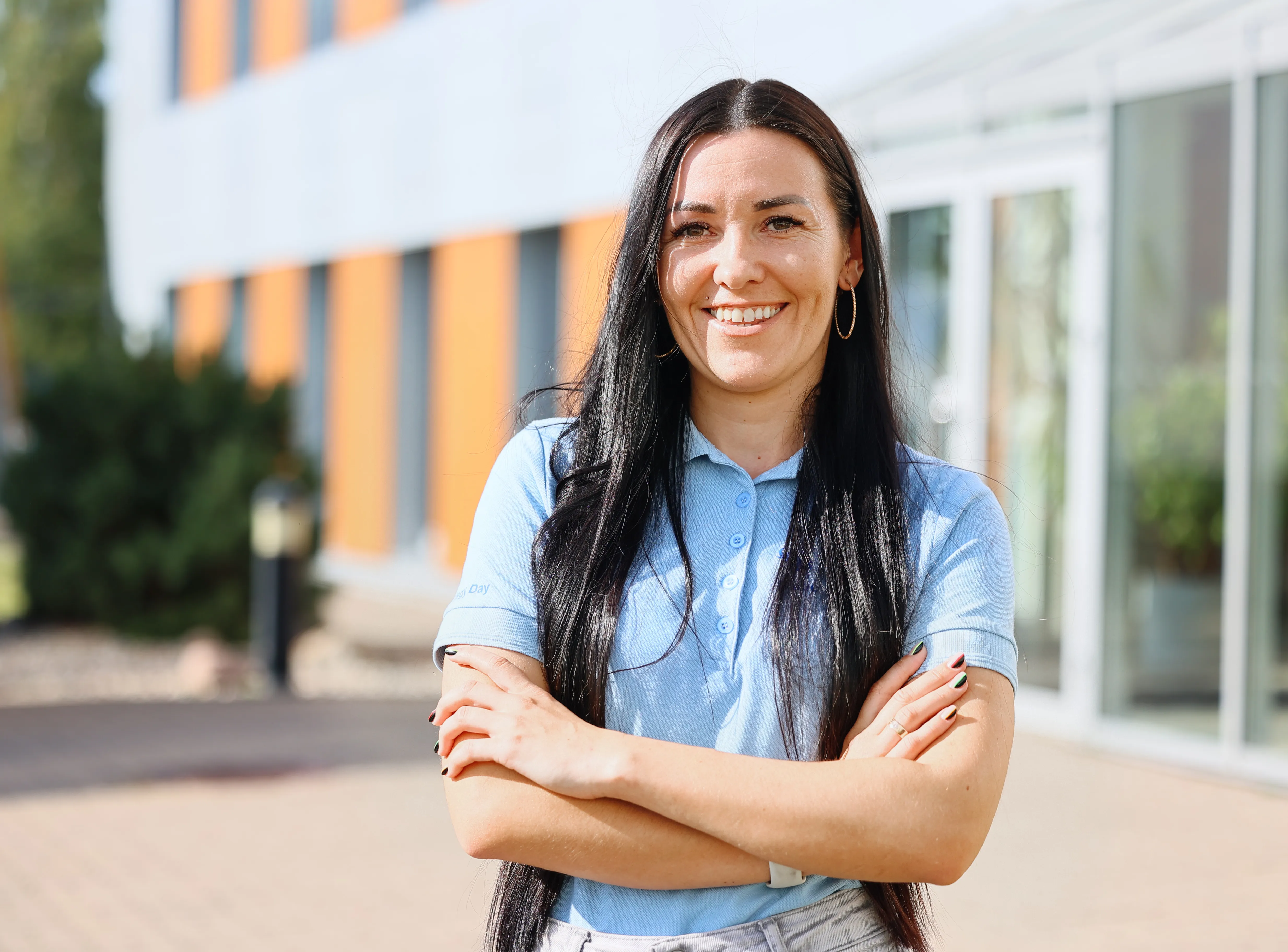 Smiling woman in a blue polo, standing confidently in front of a Schmitz Cargobull AG building, ready to drive the future of automotive.