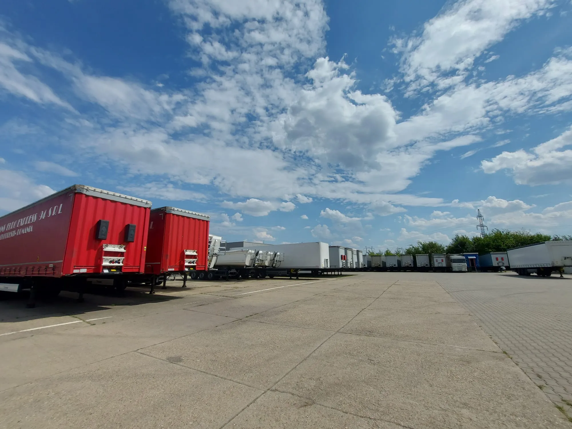A sunny day at Schmitz Cargobull AG with rows of red and white trailers parked on a spacious lot.