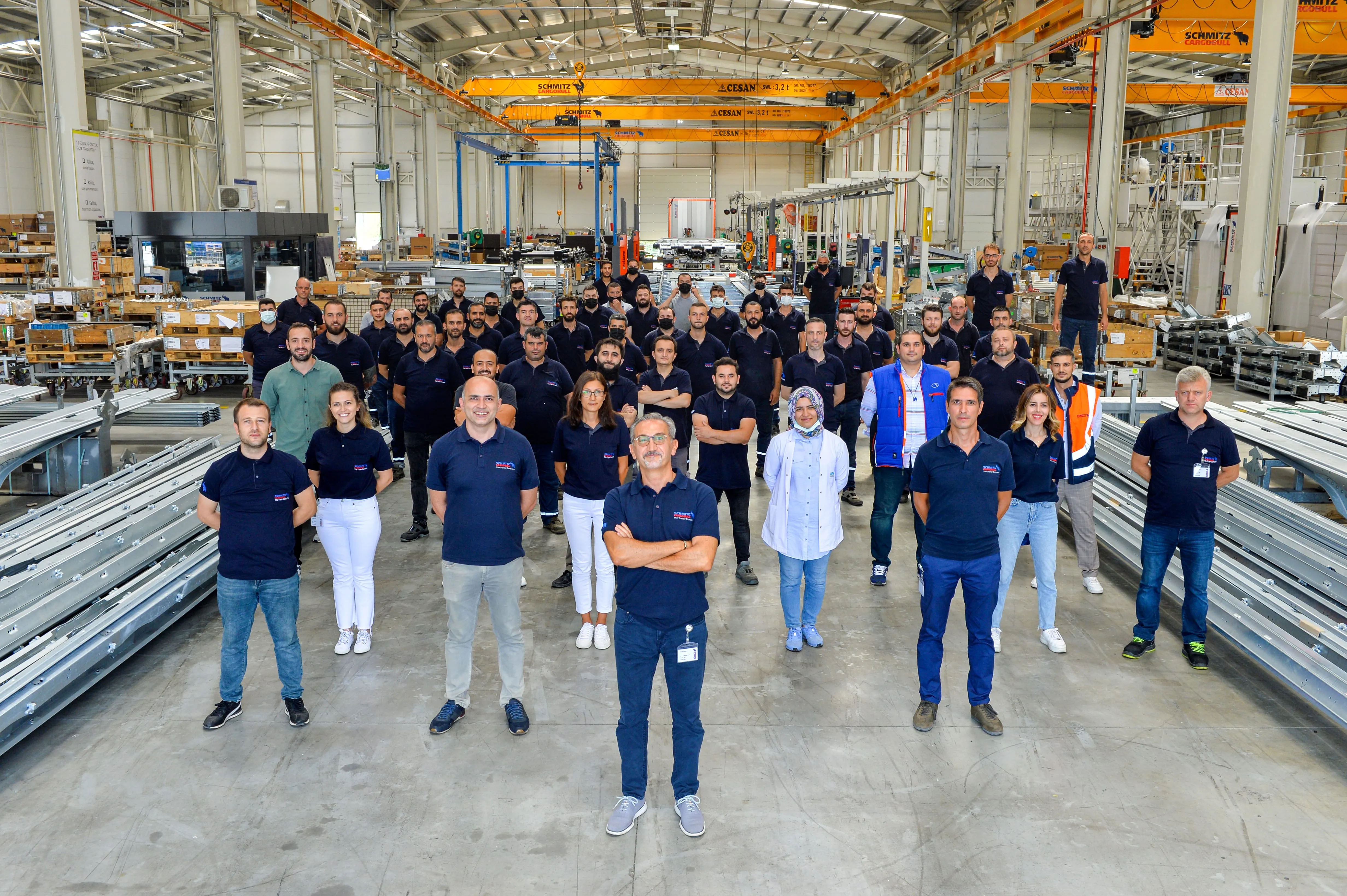 A vibrant team at Schmitz Cargobull AG posing confidently in a bustling automotive factory.