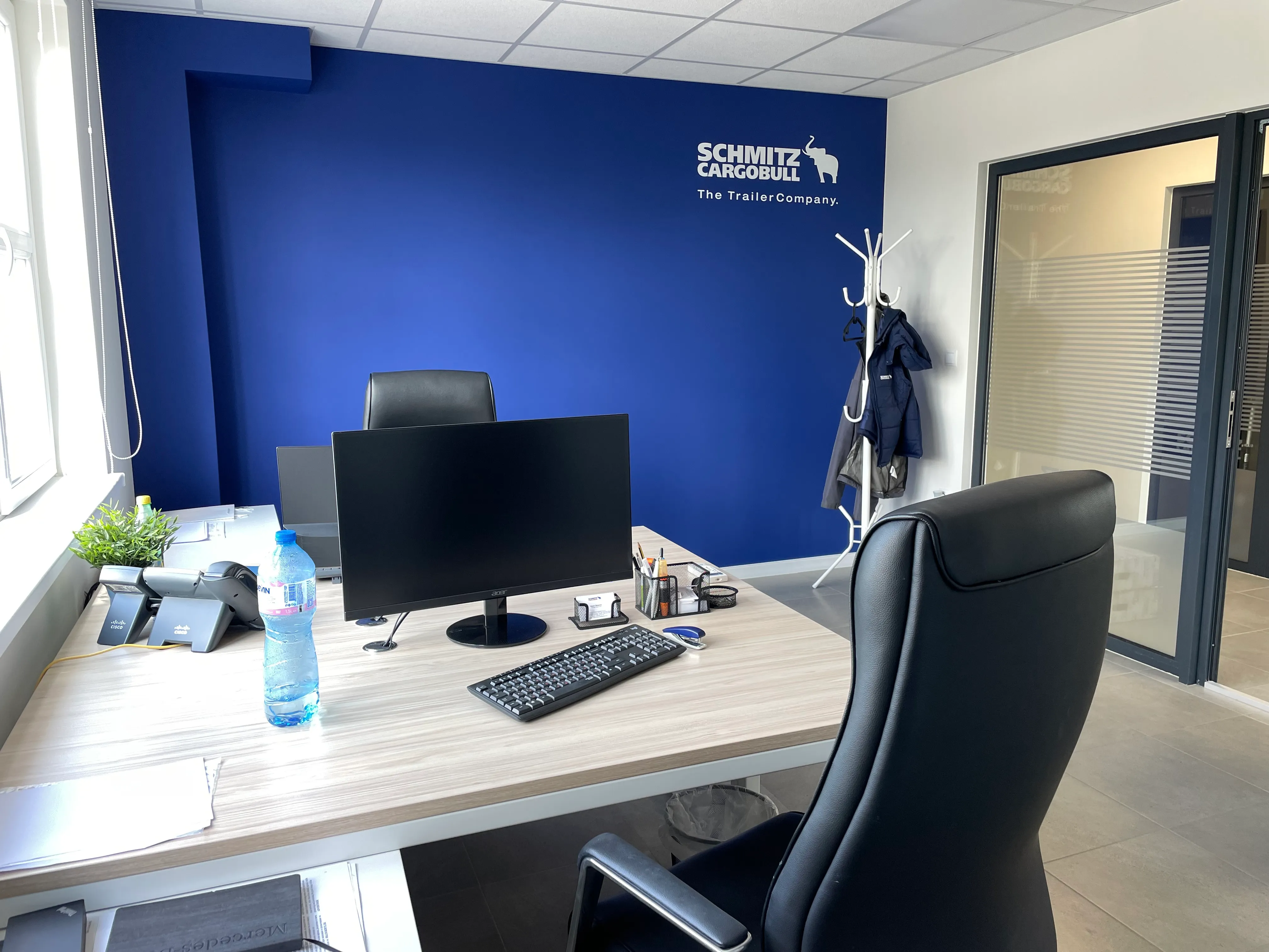 Modern office at Schmitz Cargobull AG with a sleek desk setup, comfy chairs, and the company logo on a blue accent wall.