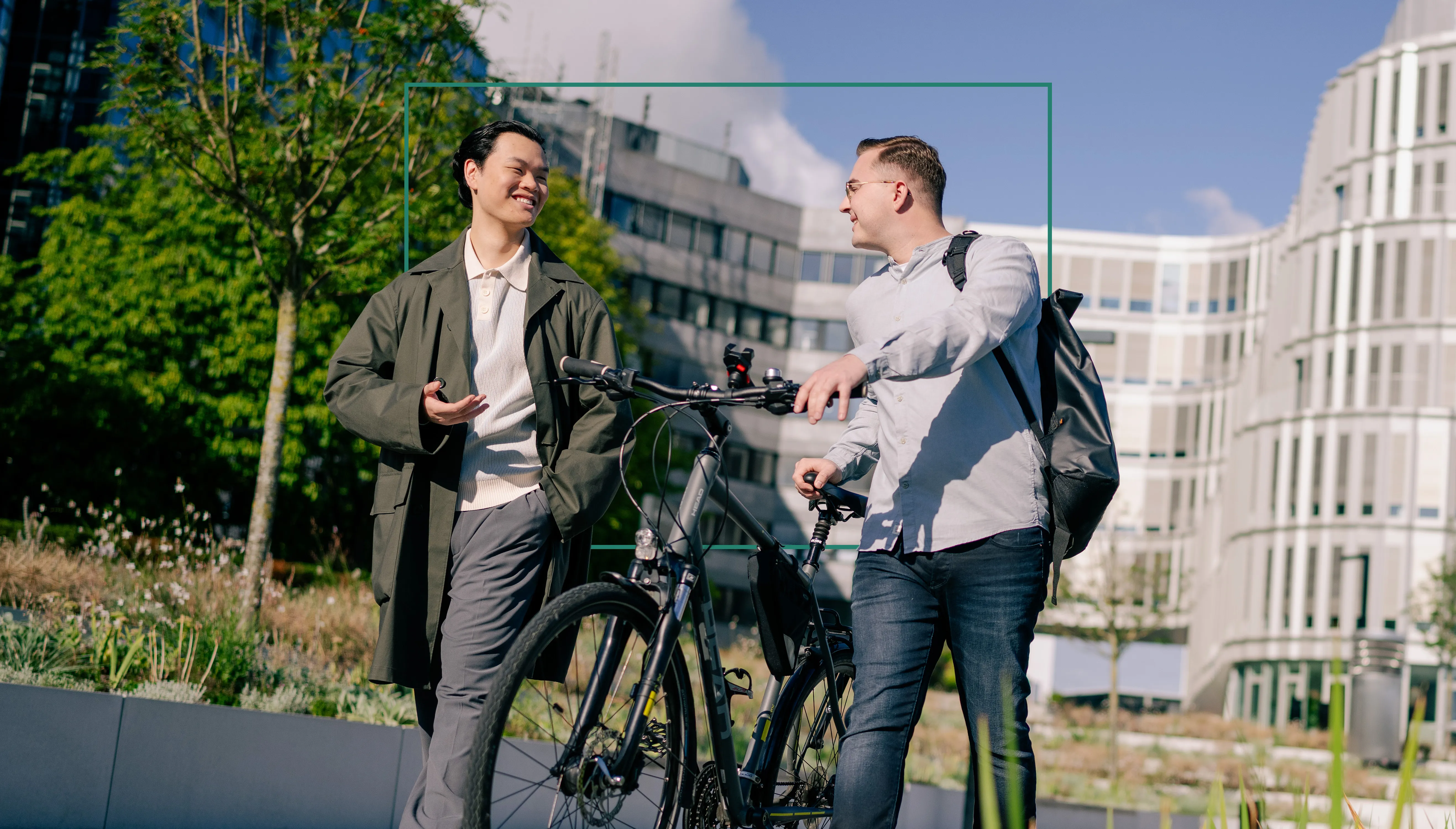 Zwei dual Studierende unterhalten sich vor dem Schüco-Gebäude. Eine Person hält ein Fahrrad.
