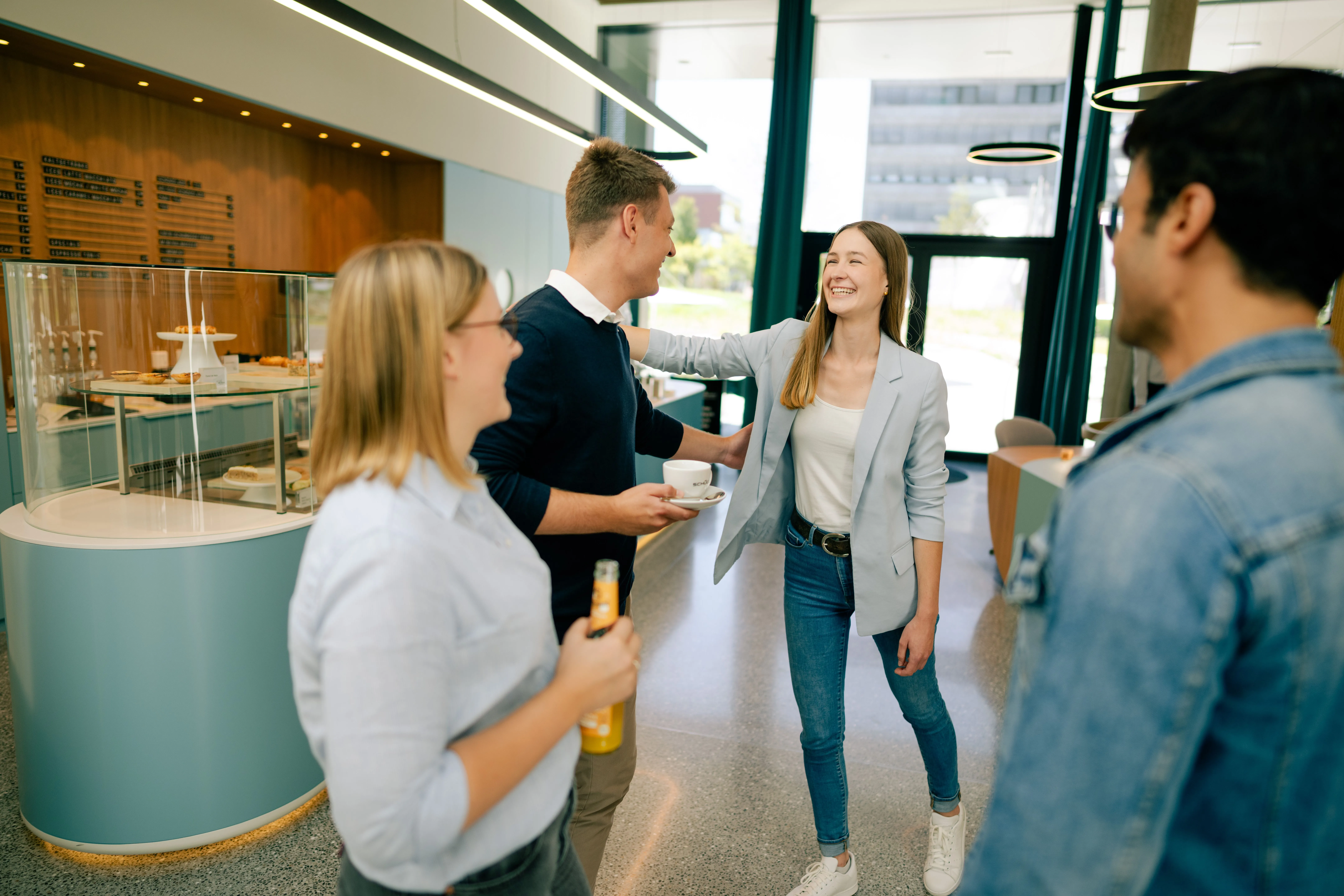 Eine Gruppe von jungen Berufstätigen genießt eine Kaffeepause in einem modernen Bürogebäude von Schüco International KG.