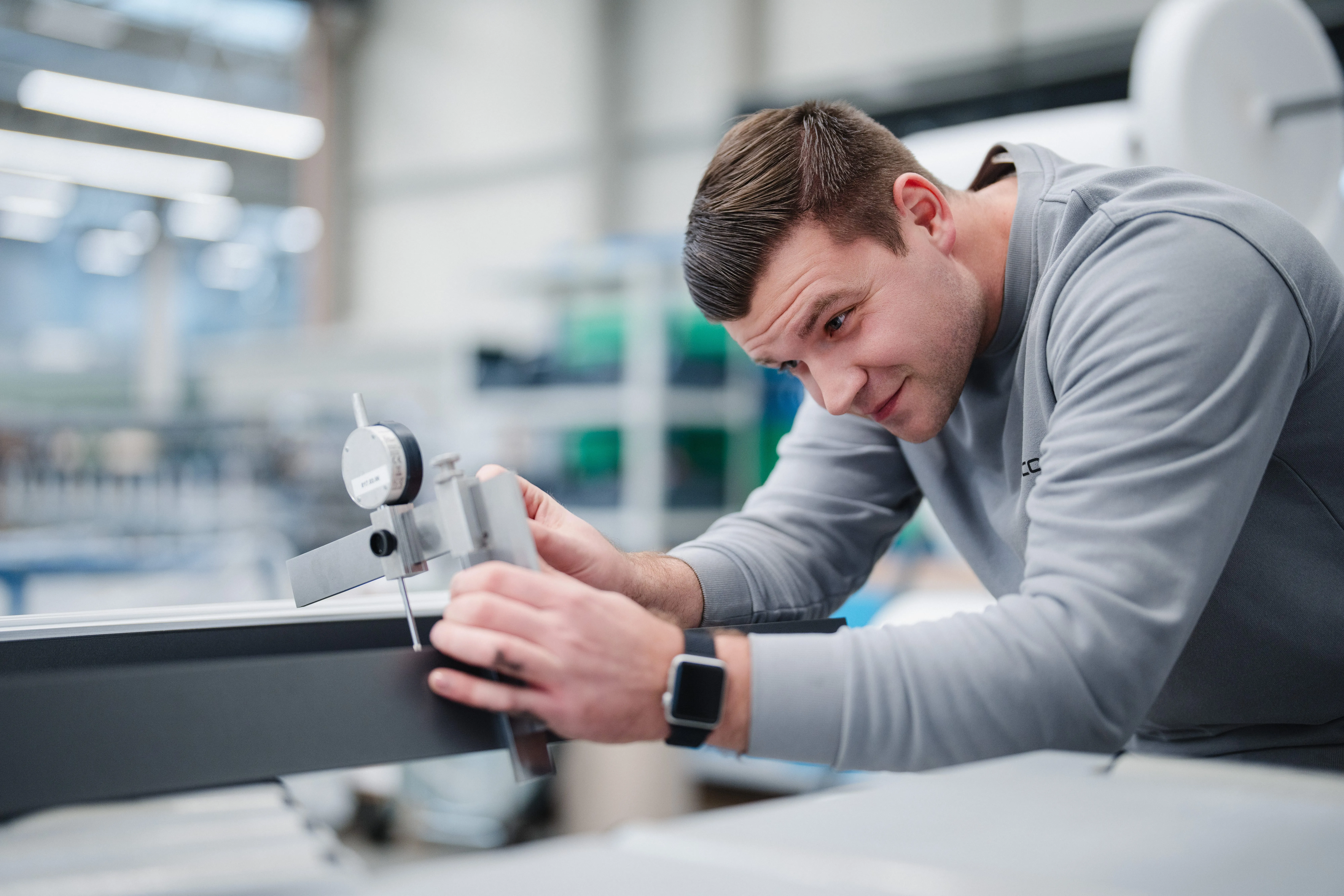 Ein junger Mann misst präzise mit einem Messgerät ein Bauteil in einer modernen Werkstatt.