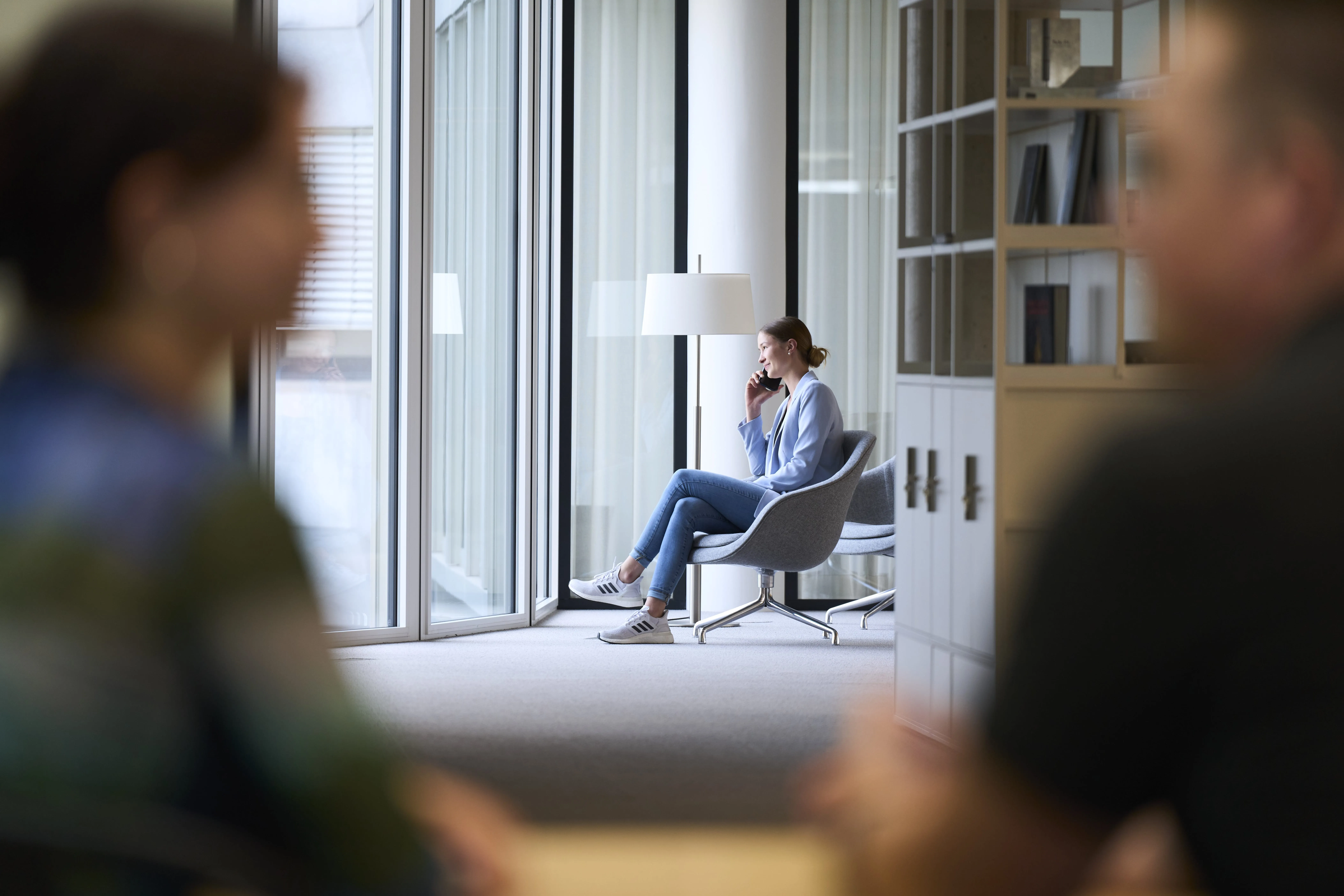 Eine Frau sitzt in einem modernen Büro und telefoniert, umgeben von großen Fenstern und zeitgenössischen Möbeln.