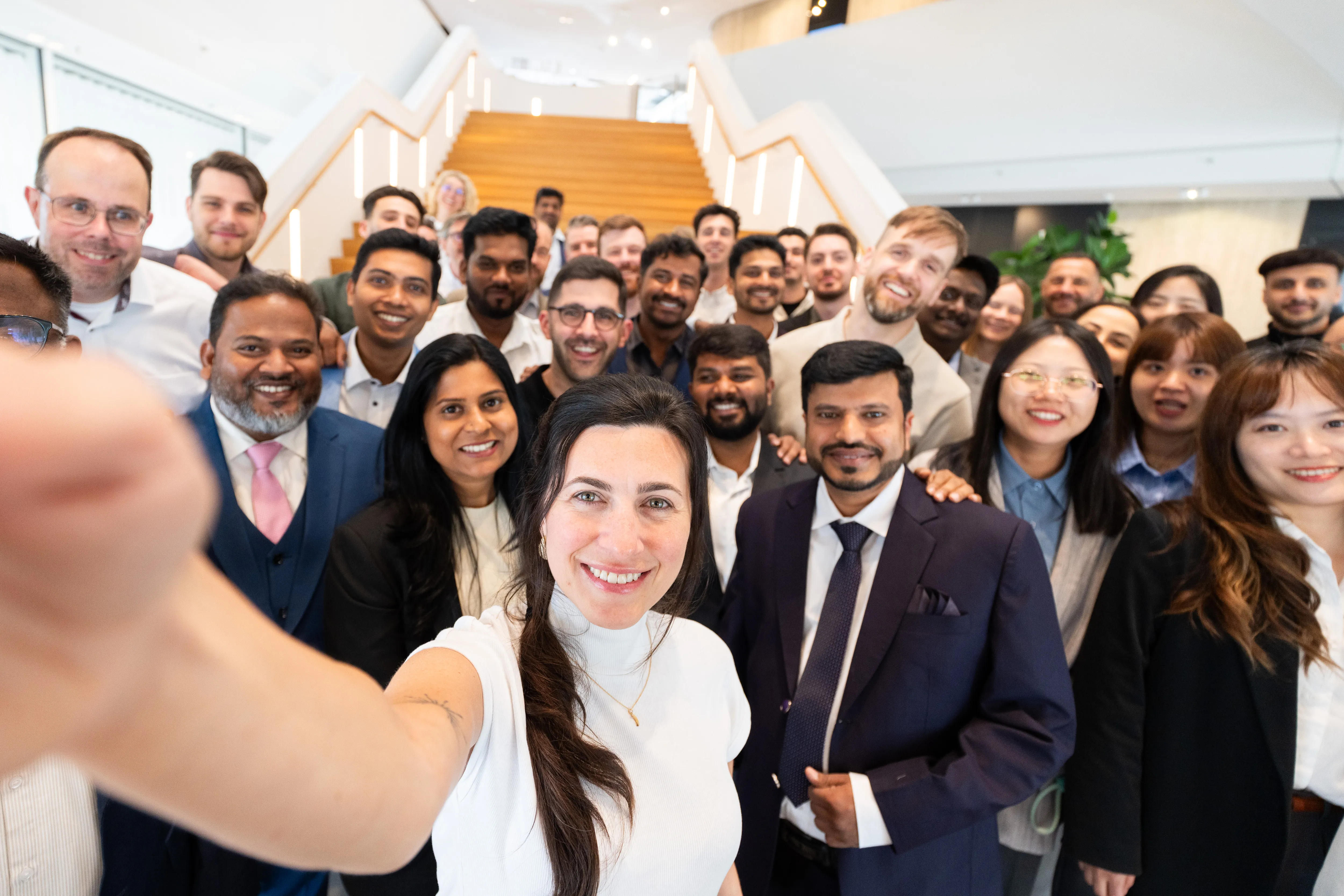 Junges, vielfältiges Team von Schüco-Mitarbeitenden macht gemeinsam ein fröhliches Gruppen-Selfie im modernen Büro.