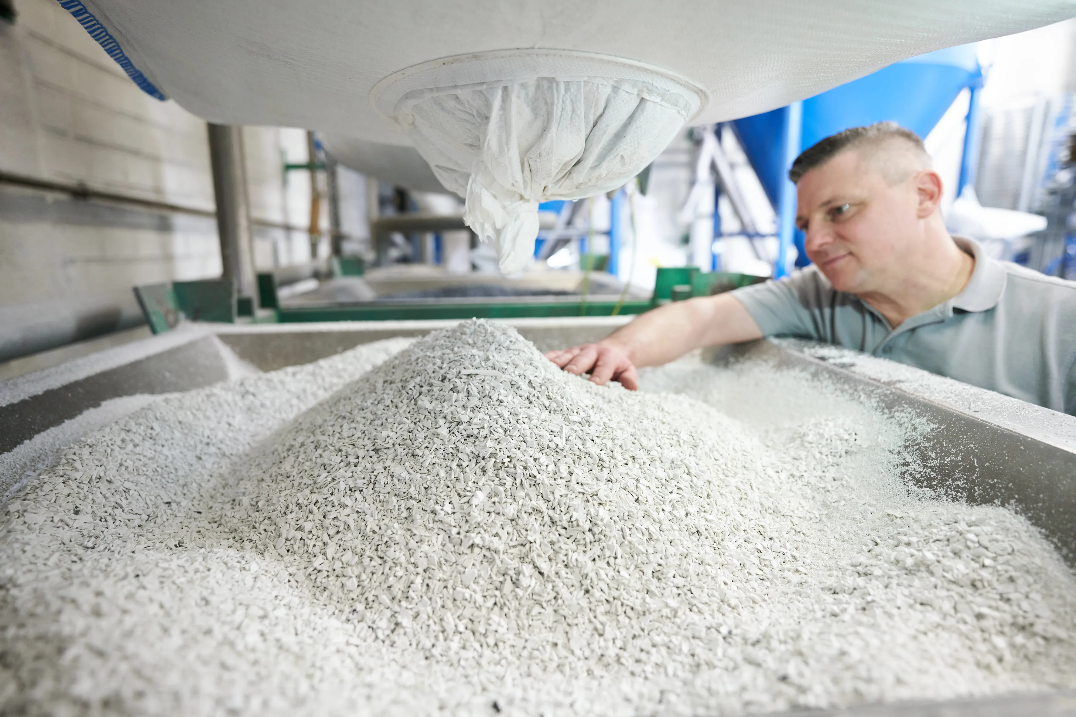 Ein Mann inspiziert ein großes Becken mit Granulat in einer Produktionsanlage von Schüco International KG.