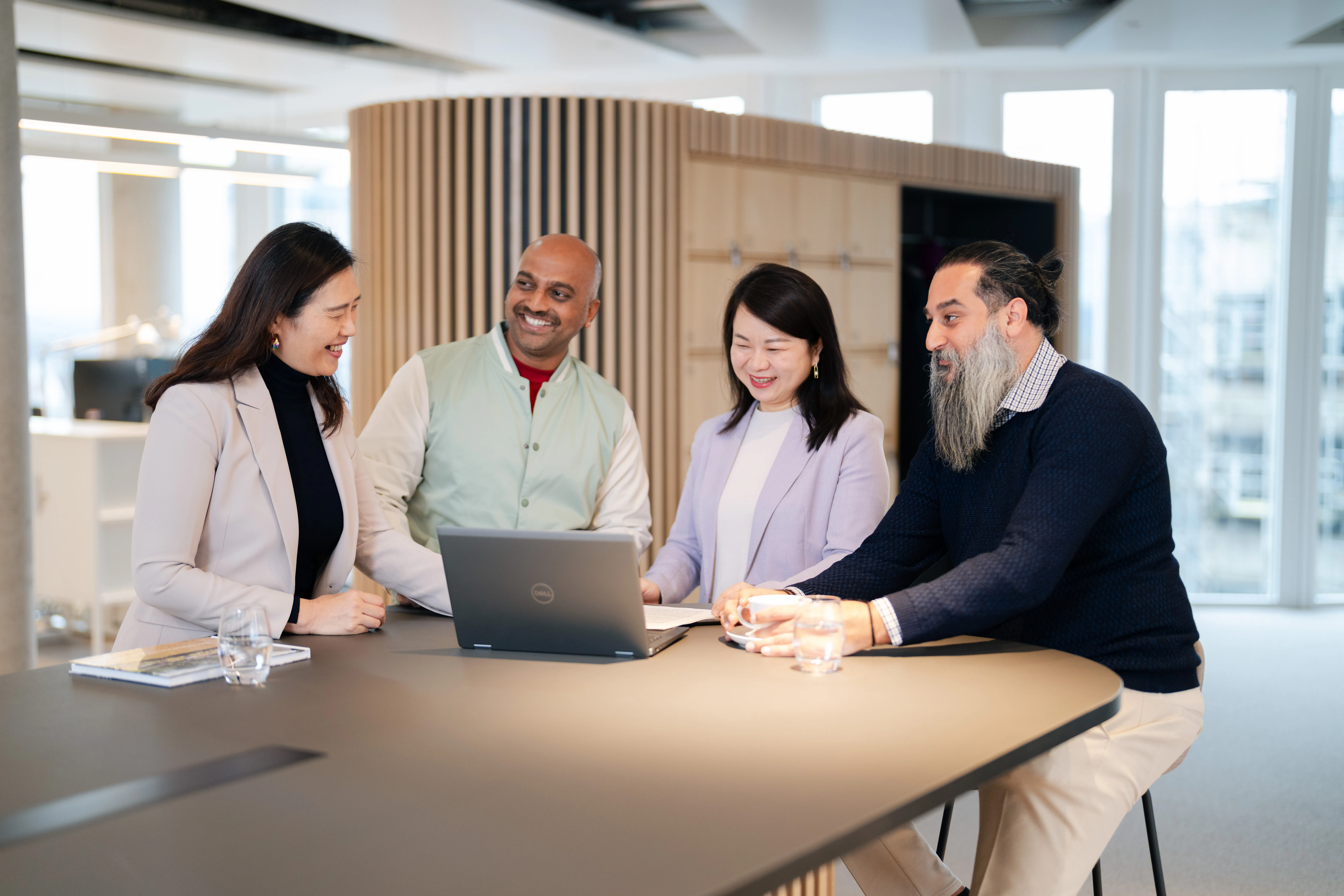 Eine Gruppe von vier Personen diskutiert freundlich an einem Tisch in einem modernen Büro bei Schüco International KG.