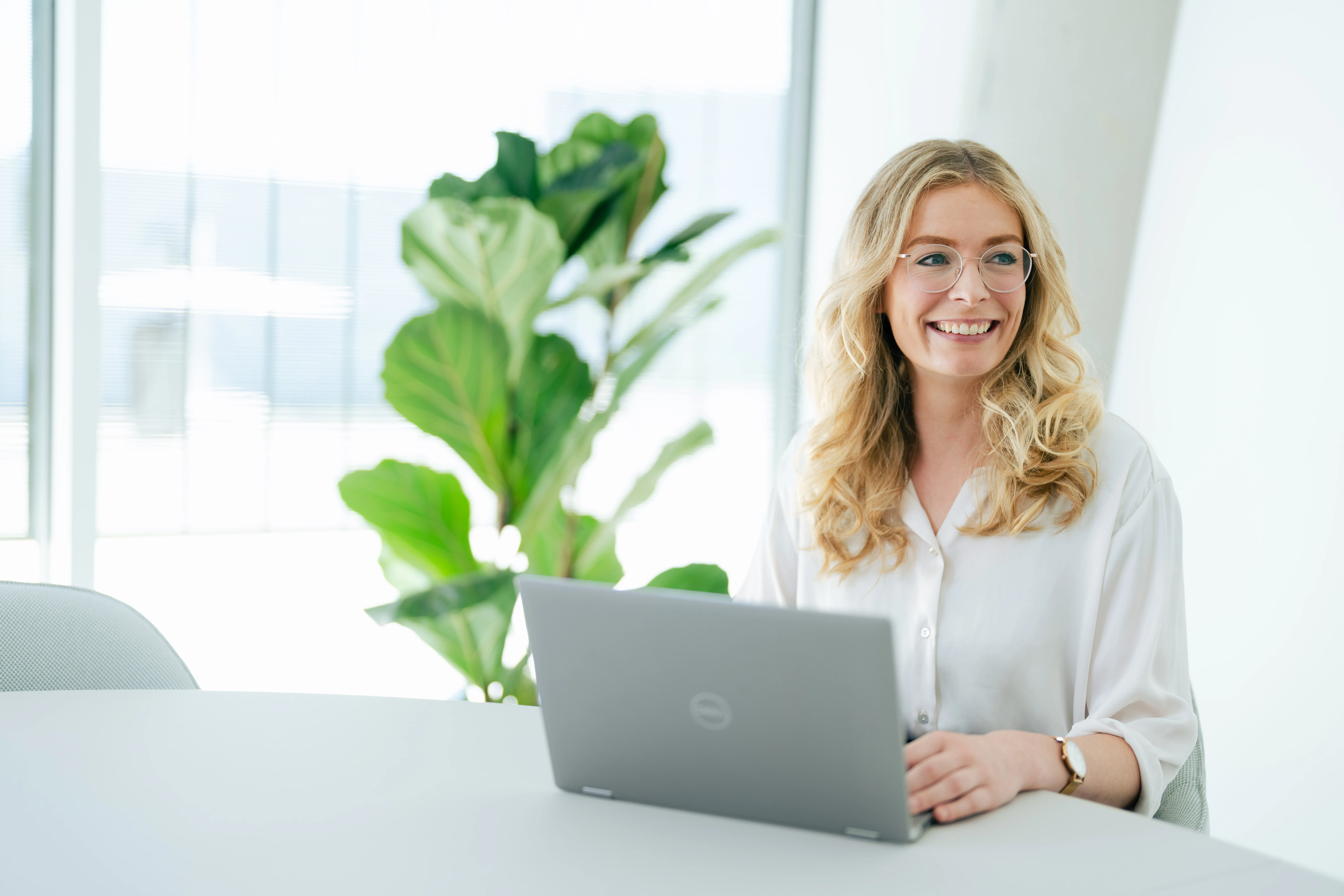 Eine lächelnde Frau arbeitet an einem Laptop in einem modernen Büro bei Schüco International KG.