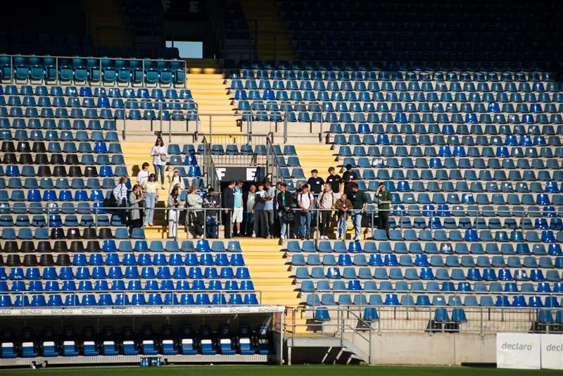 Eine Gruppe von Menschen in der Schüco-Arena, umgeben von leeren blauen Sitzreihen bei Sonnenschein.