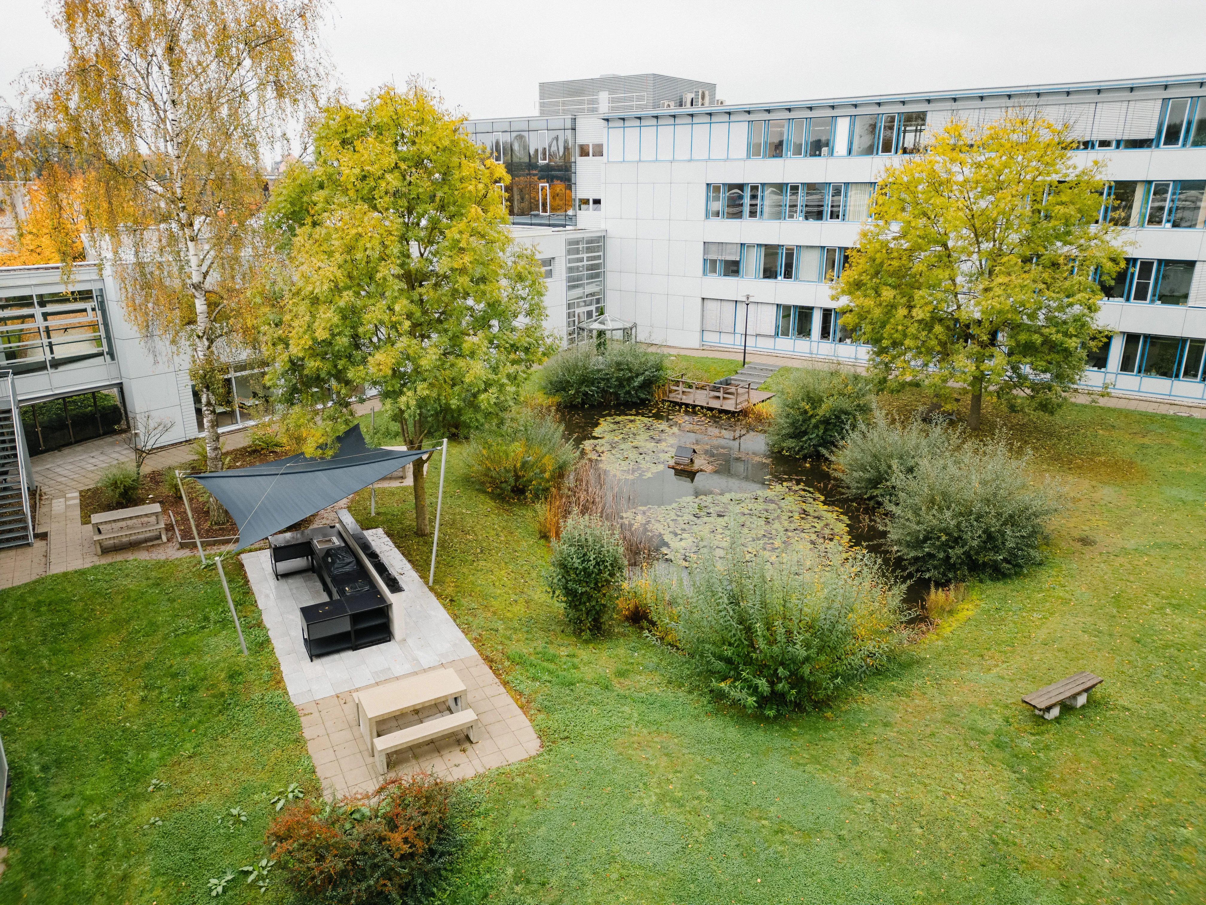 Ein grüner Innenhof bei Schüco mit Teich, Sitzbereich und moderner Architektur im Hintergrund.