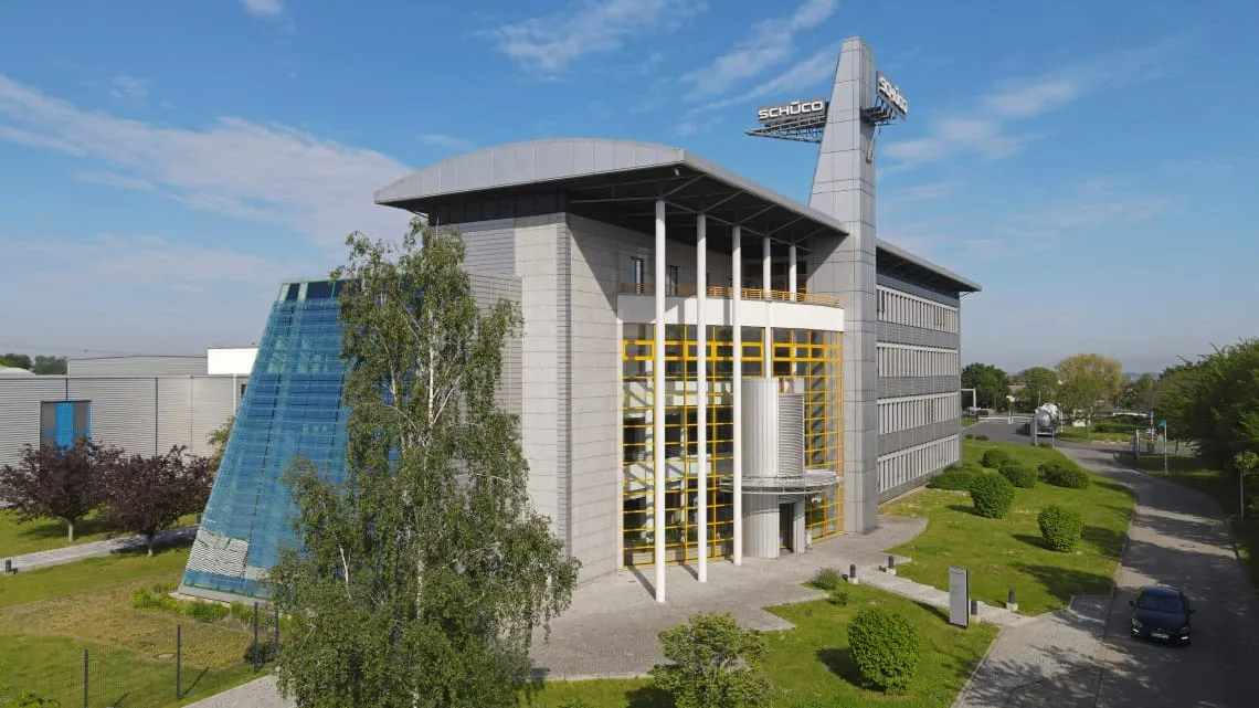 Gebäude des Schüco International KG mit moderner Architektur und Glasfassade, umgeben von Grünflächen und einem klaren Himmel.