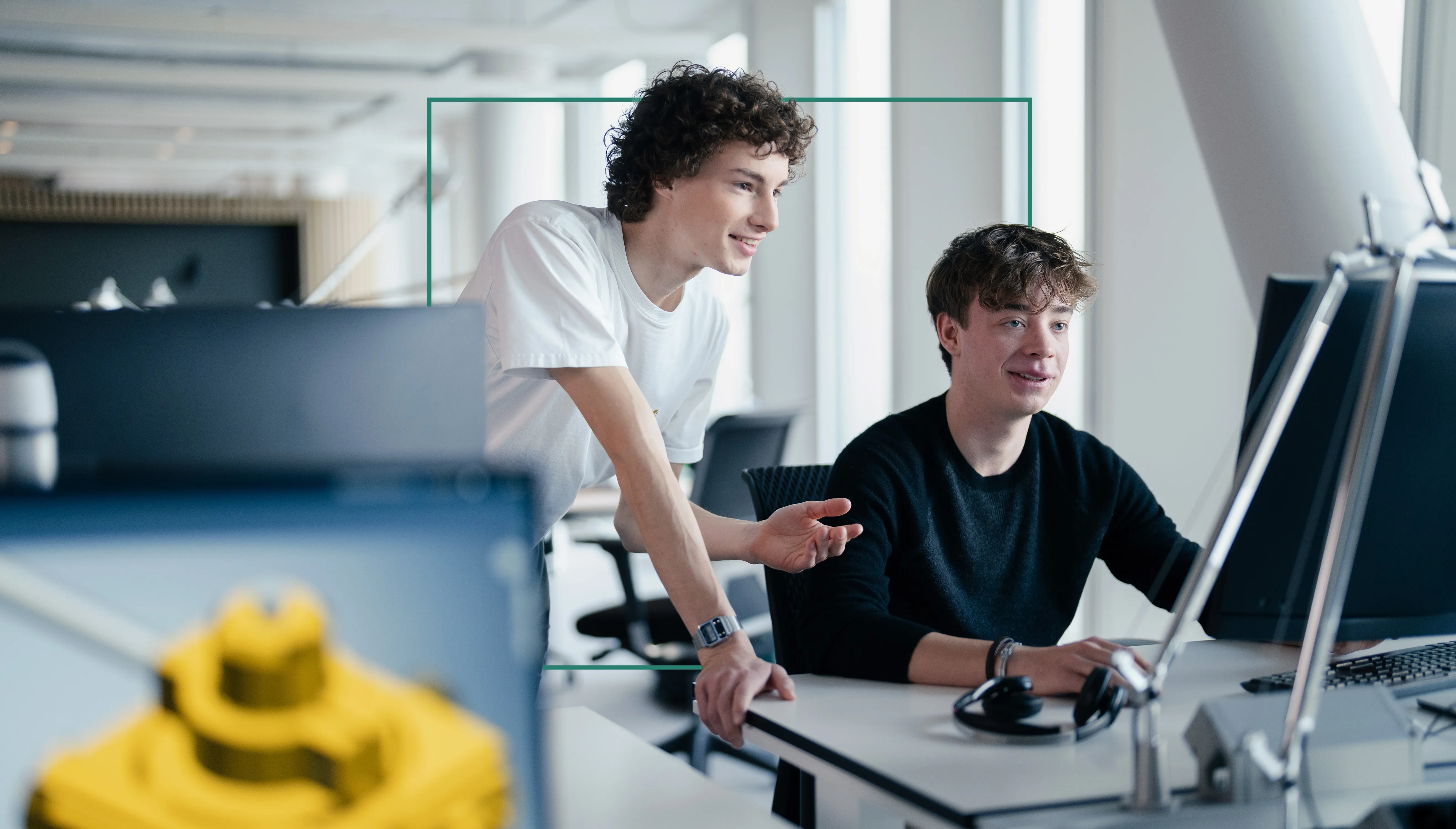 Ein Auszubildender sitzt mit einem Schüler in einem Schülerpraktikum vor einem PC und erklärt ihm technische Zeichnungen.