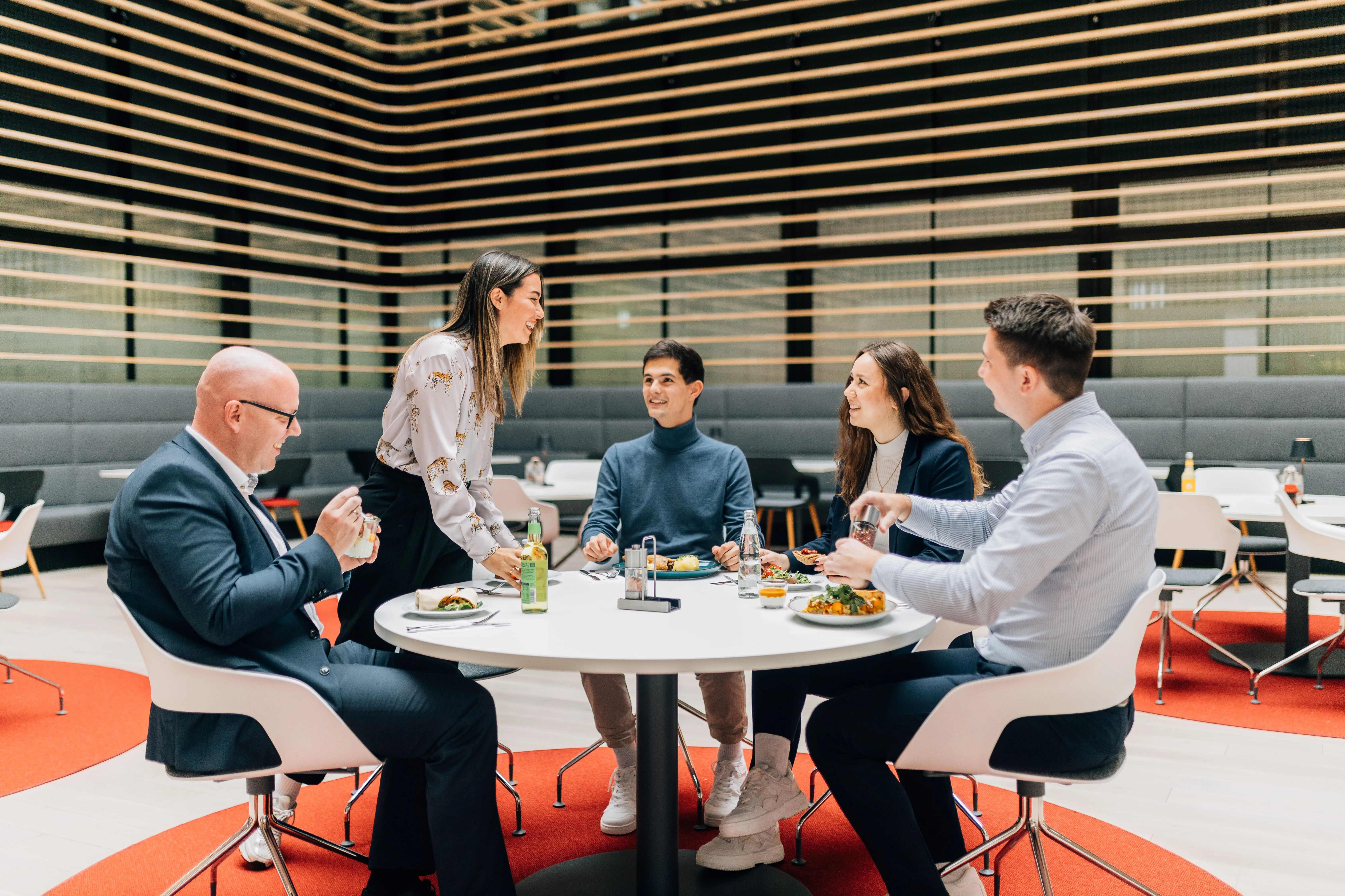 Eine Gruppe von fünf Kolleg*innen der Sparkasse Bielefeld hat eine entspannte Mittagspause in einer modernen Kantine.