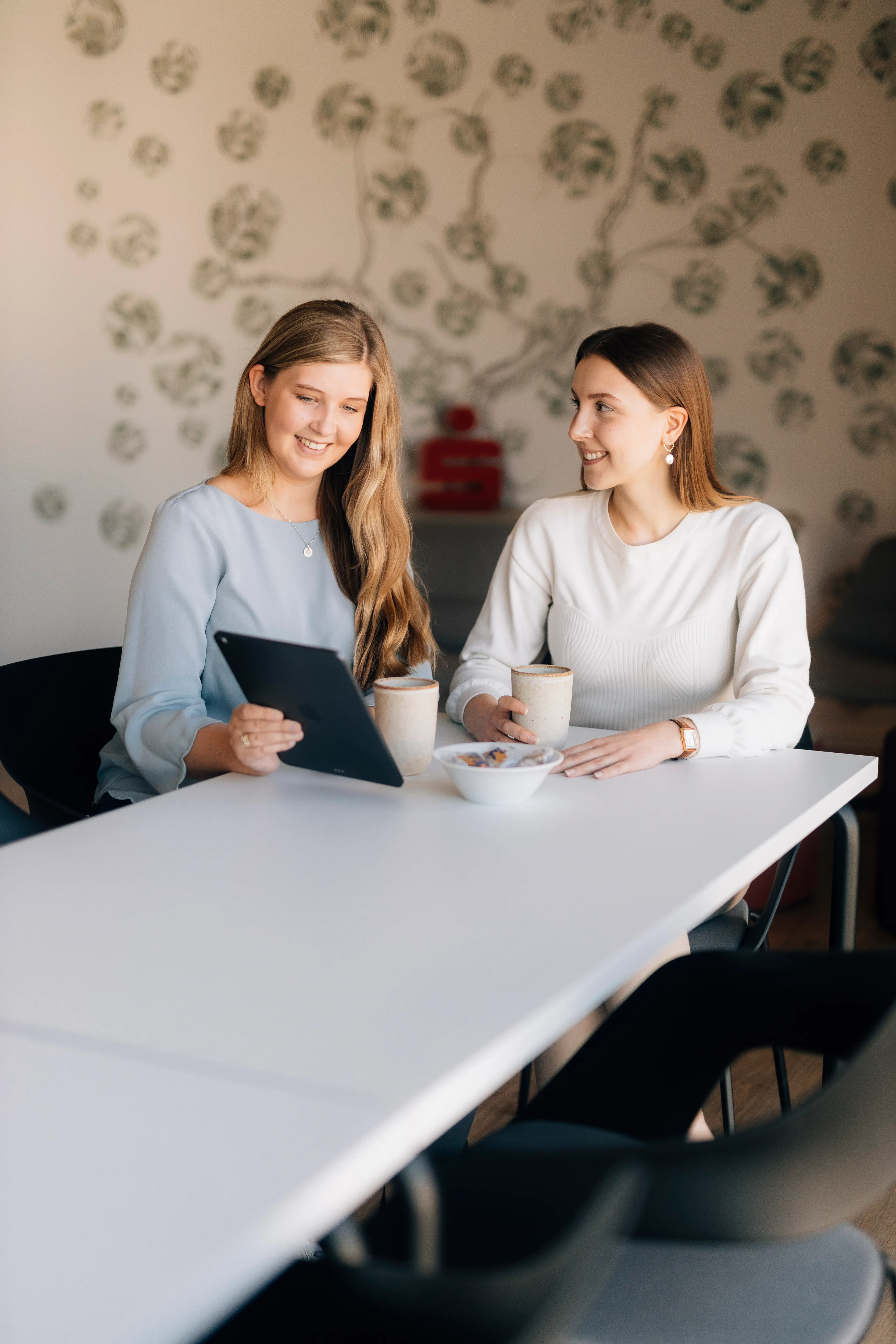 Zwei Frauen trinken Kaffee und schauen gemeinsam auf ein Tablet in einem modernen Büro bei Sparkasse Bielefeld.