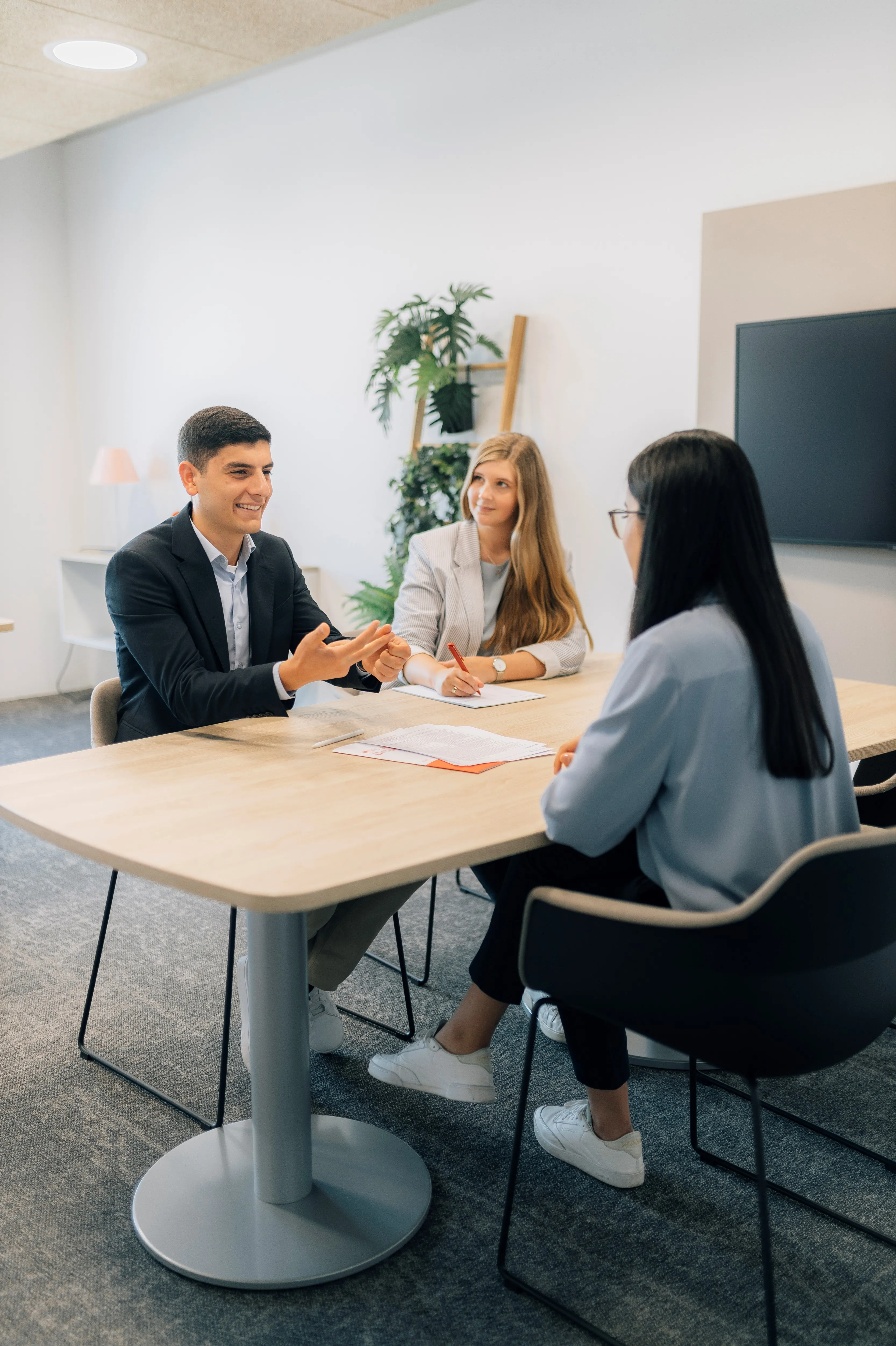 Drei Personen in einem modernen Büro, die ein Bewerbungsgespräch führen. Eine Person spricht, zwei hören aufmerksam zu.