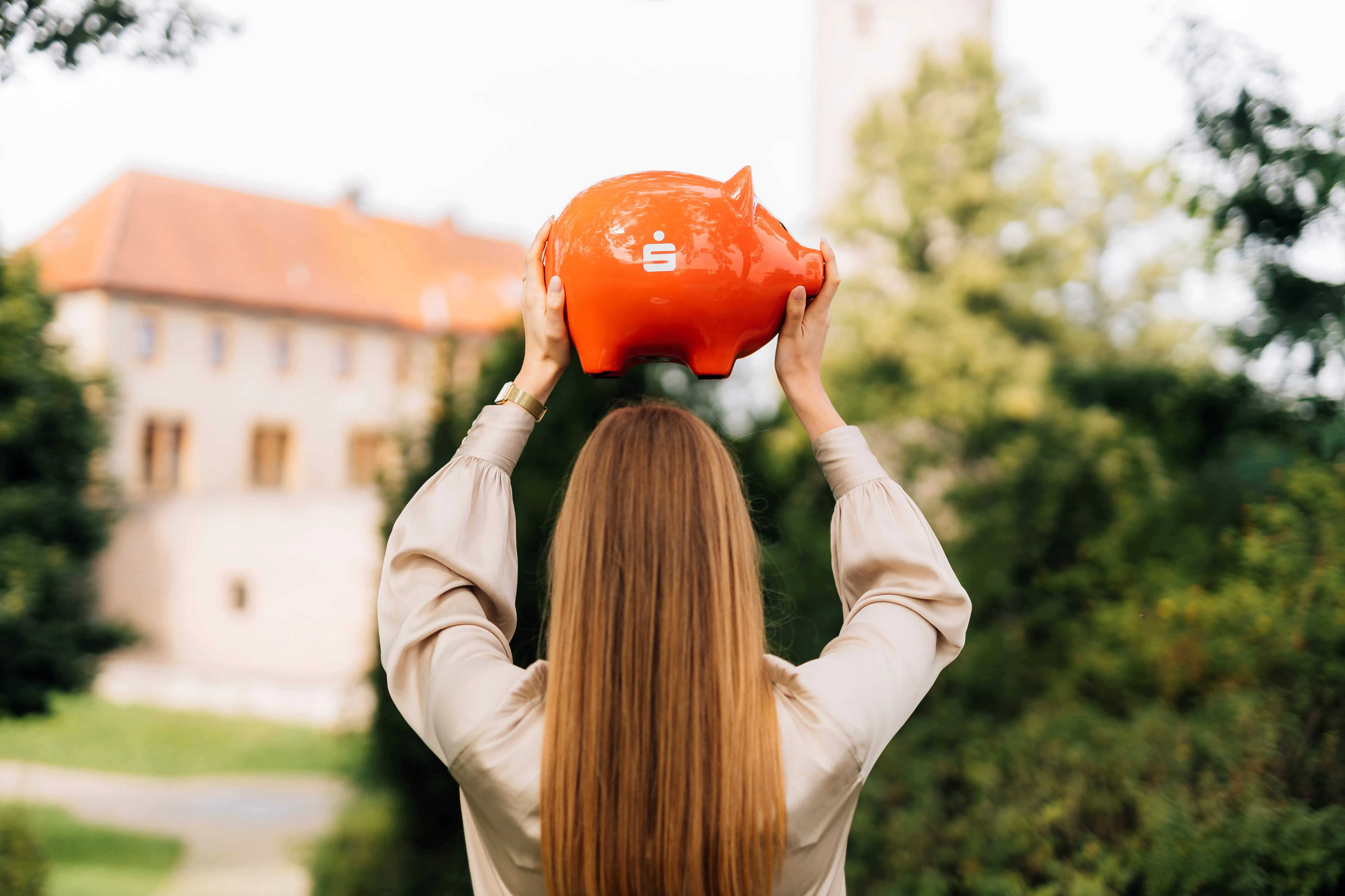 Eine lächelnde Frau im Anzug hält eine "Top Company 2025"-Auszeichnung von Kununu. Sie sitzt lässig draußen auf einer Bank.