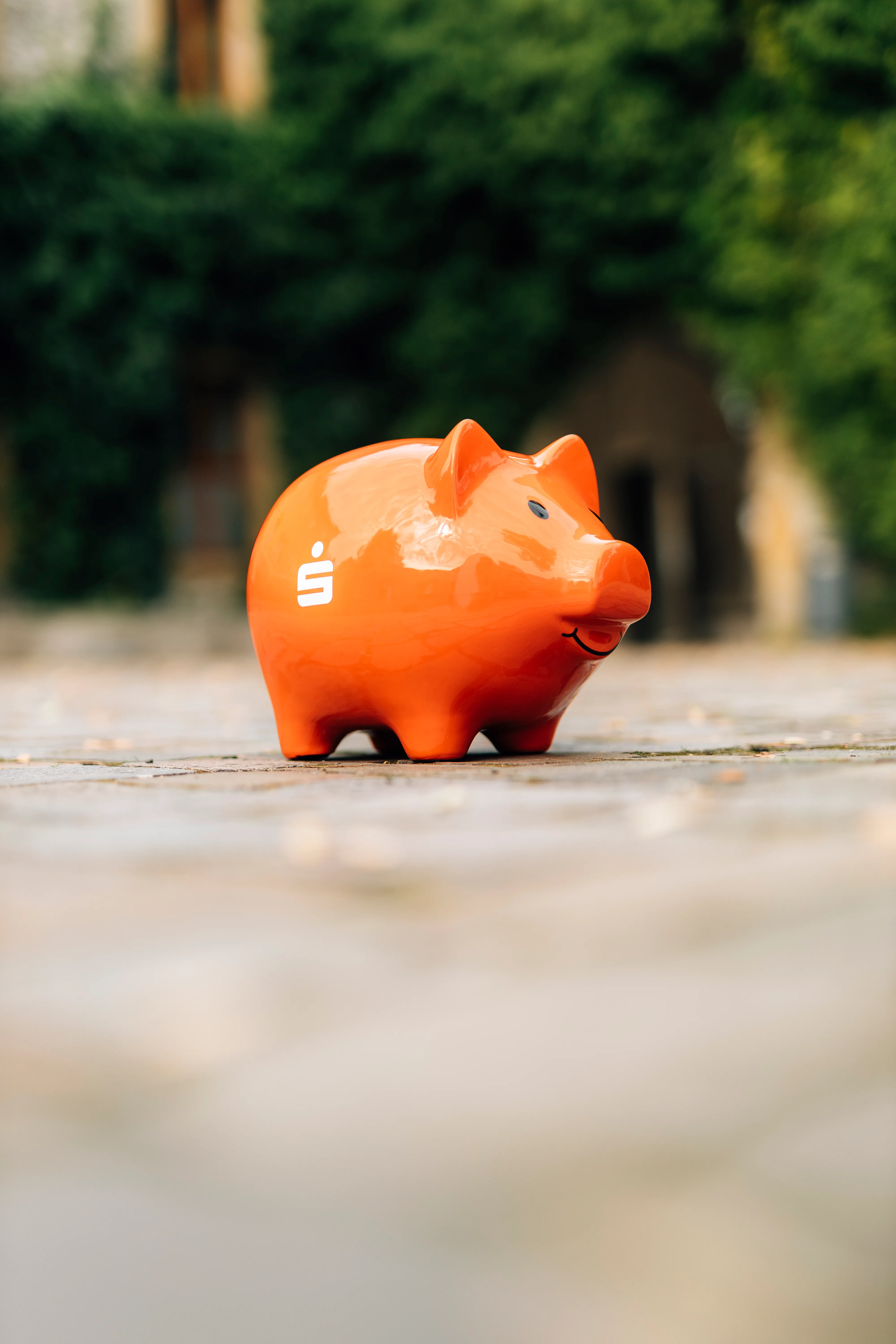 Ein rotes Sparschwein mit Sparkassen-Logo steht auf einem gepflasterten Weg.