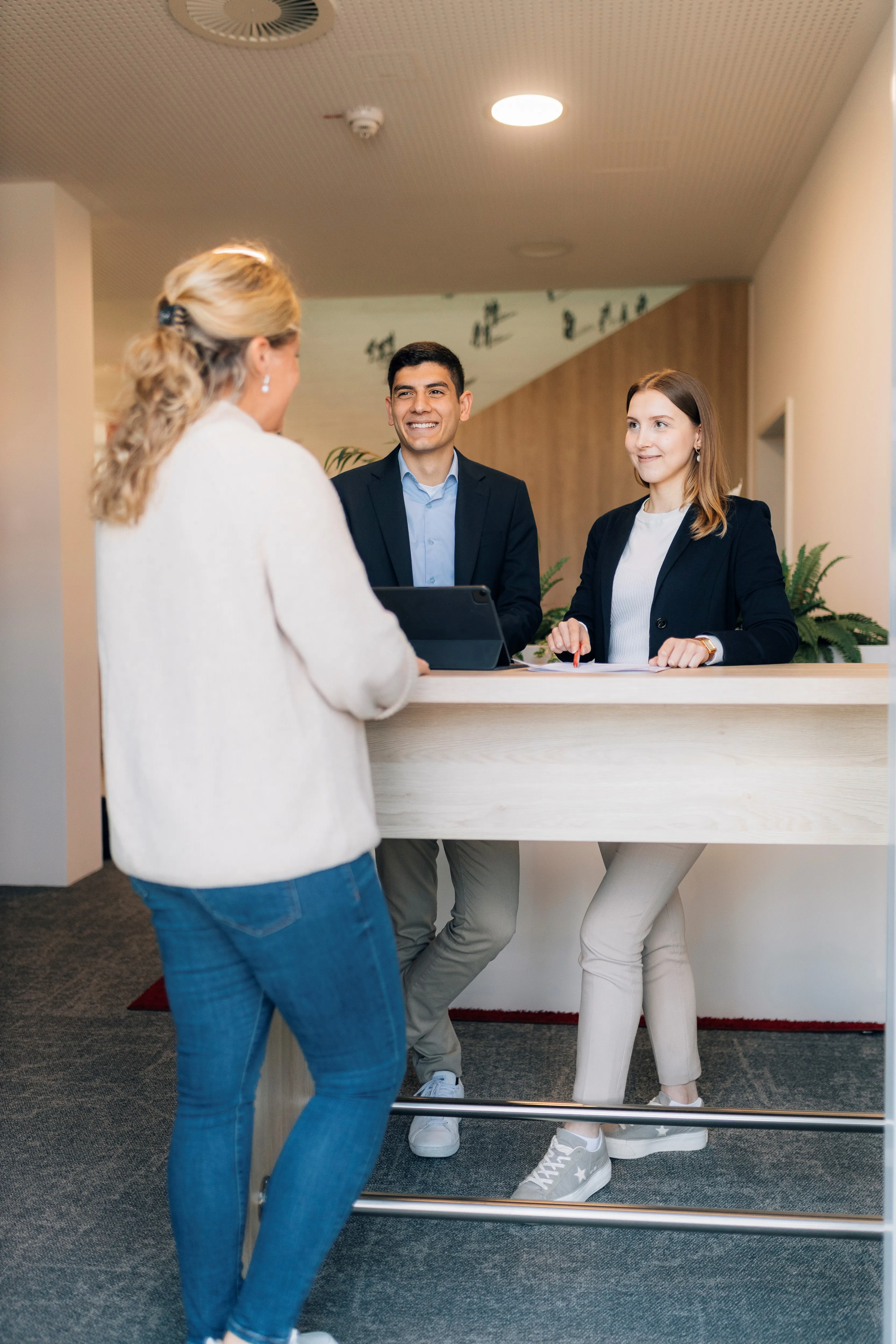 Eine Frau spricht mit zwei Mitarbeiter:innen der Sparkasse Bielefeld am Empfangstresen. Sie lächeln freundlich.