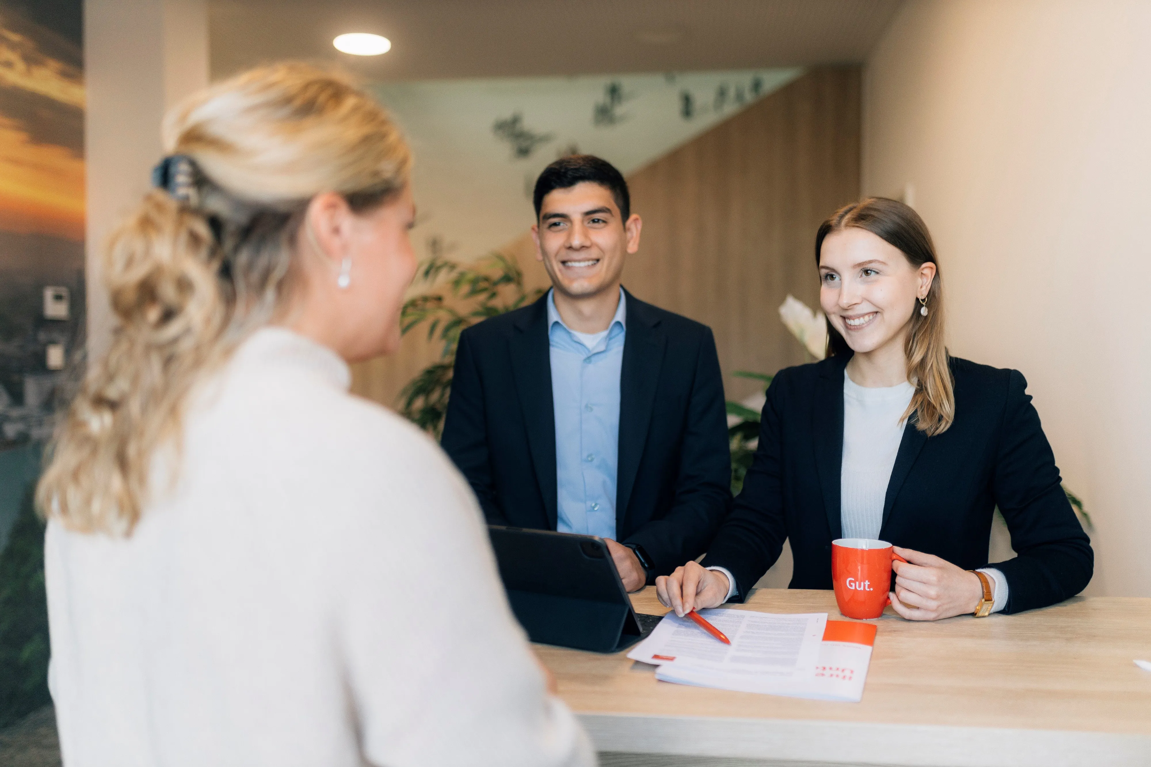 Zwei Bankmitarbeiter der Sparkasse Bielefeld begrüßen eine Kundin am Empfangstresen mit freundlichen Gesichtern.