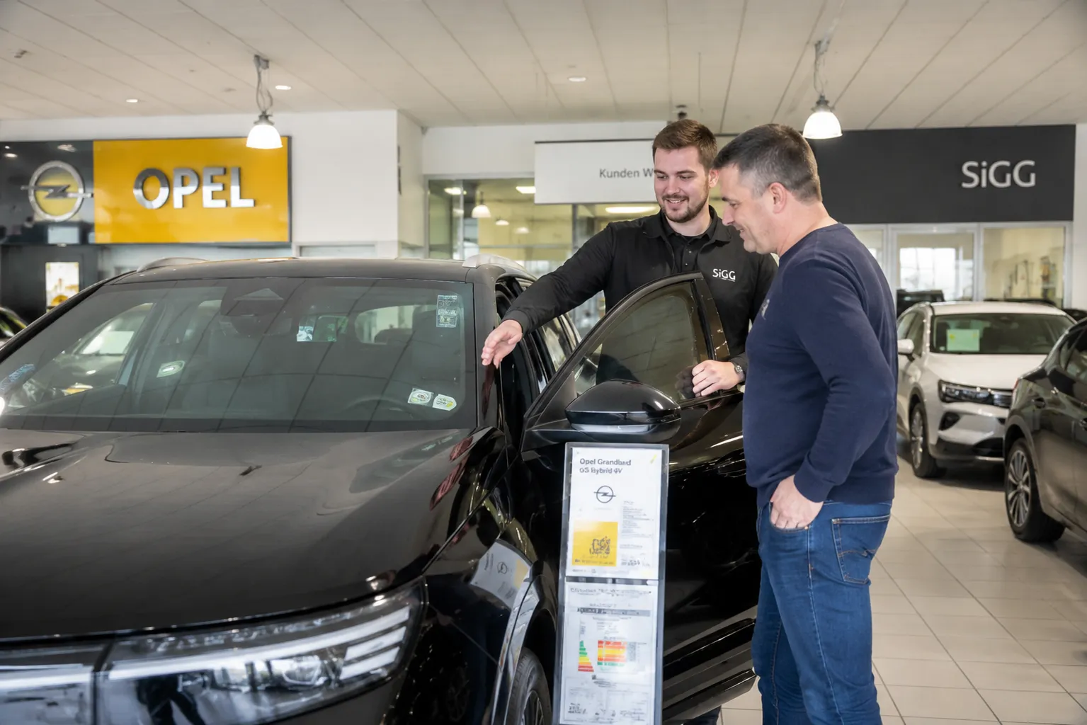 Ein Verkaufsberater zeigt Dir im Autohaus ein Opel-Fahrzeug und erklärt Details zum Modell.