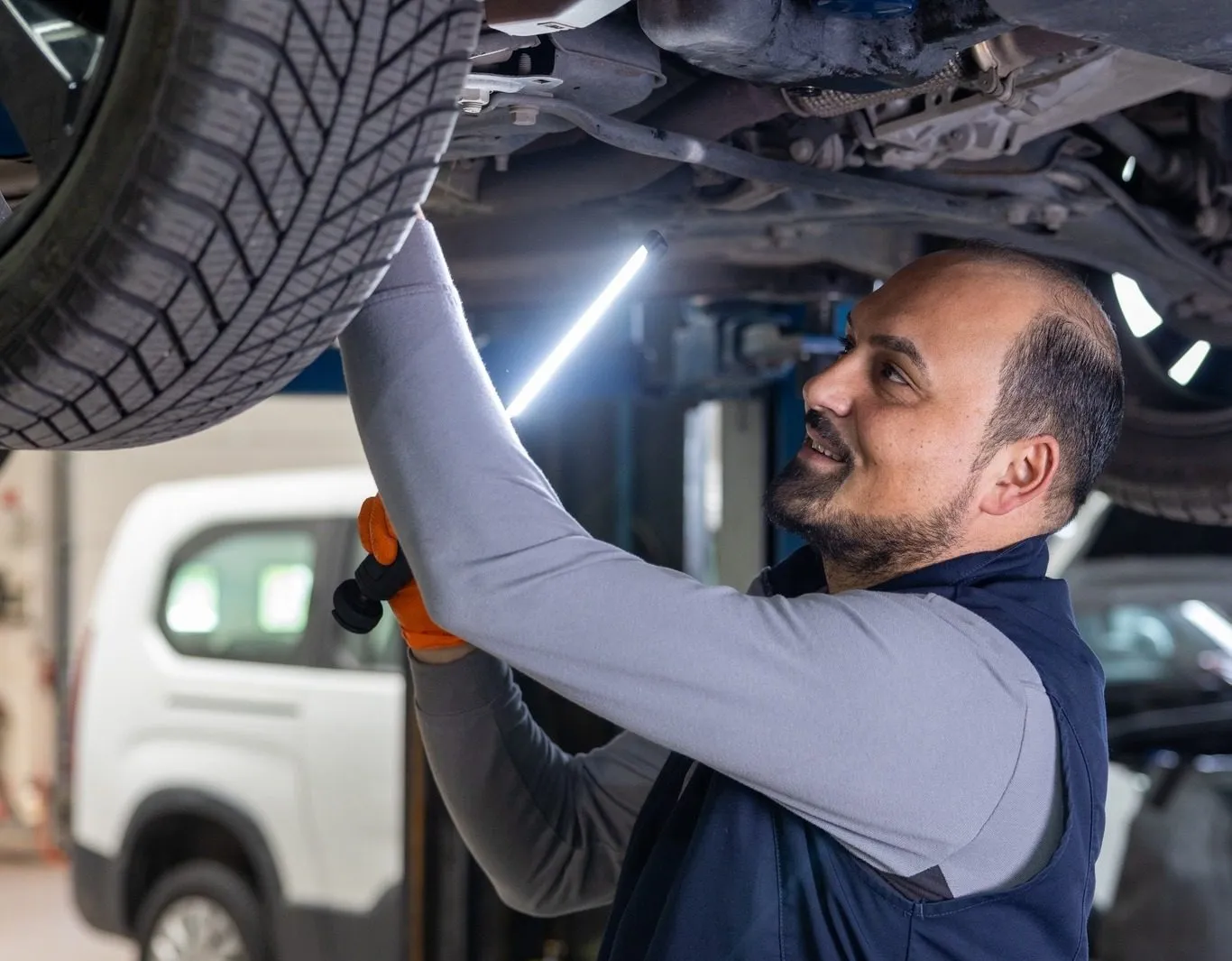 Ein Mechaniker arbeitet lächelnd unter einem Auto in einer Werkstatt.