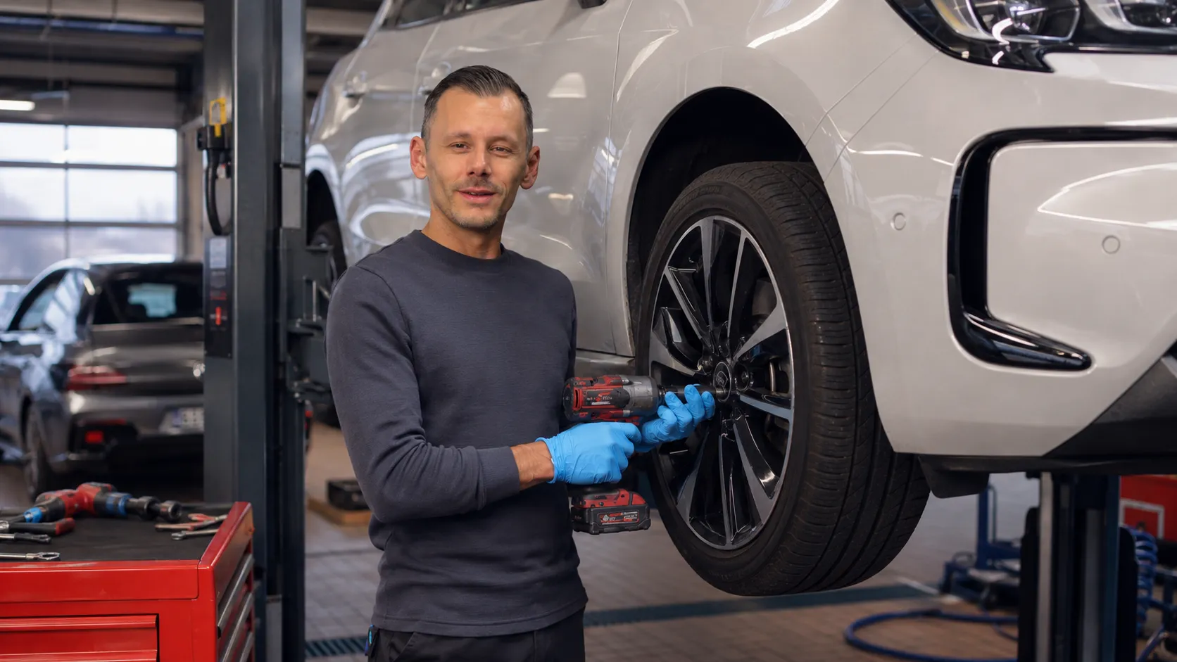 Ein Kfz-Mechatroniker arbeitet mit Handschuhen an einem Auto auf der Hebebühne in einer Stellantis Werkstatt.