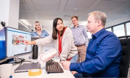 Ein Team von vier Kollegen bespricht ein Projekt am Computer in einem modernen Büro.