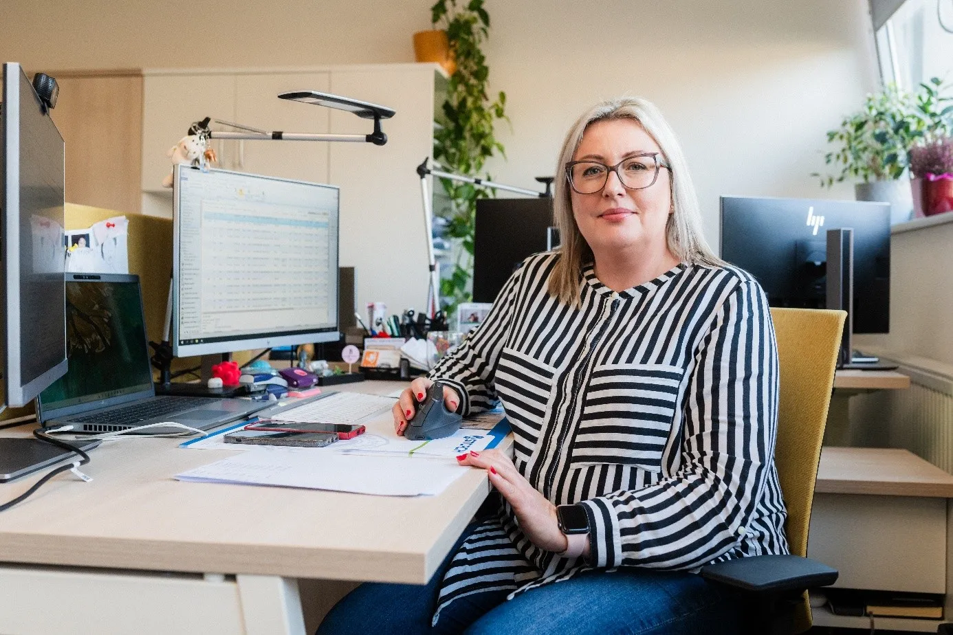 Ein lächelnder Mann in einem Serverraum hält einen Laptop in der Hand.